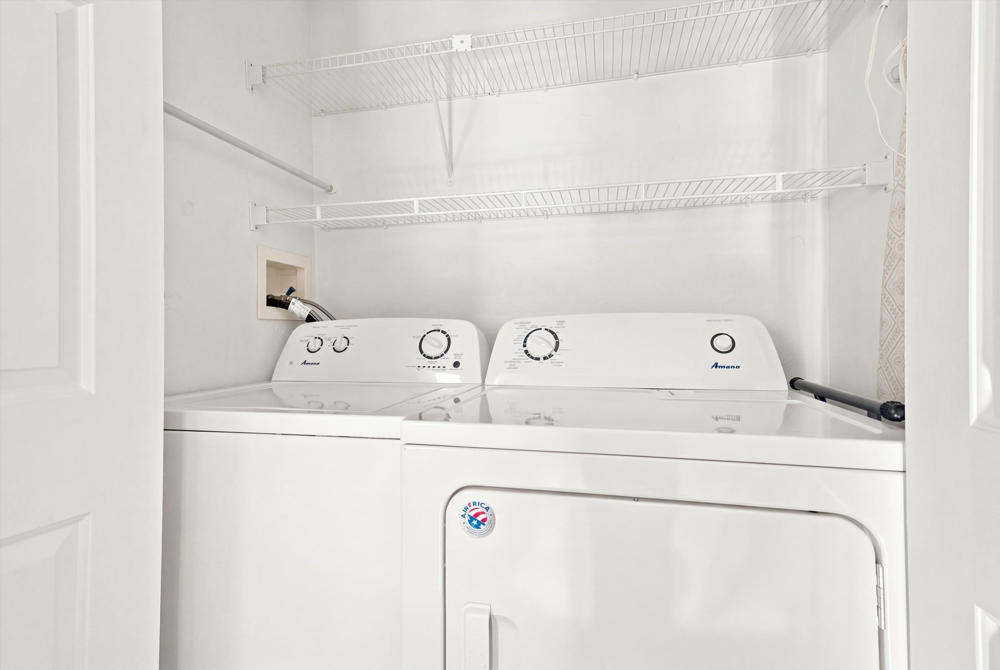 Laundry closet with side-by-side white washer and dryer beneath wire storage shelves.
