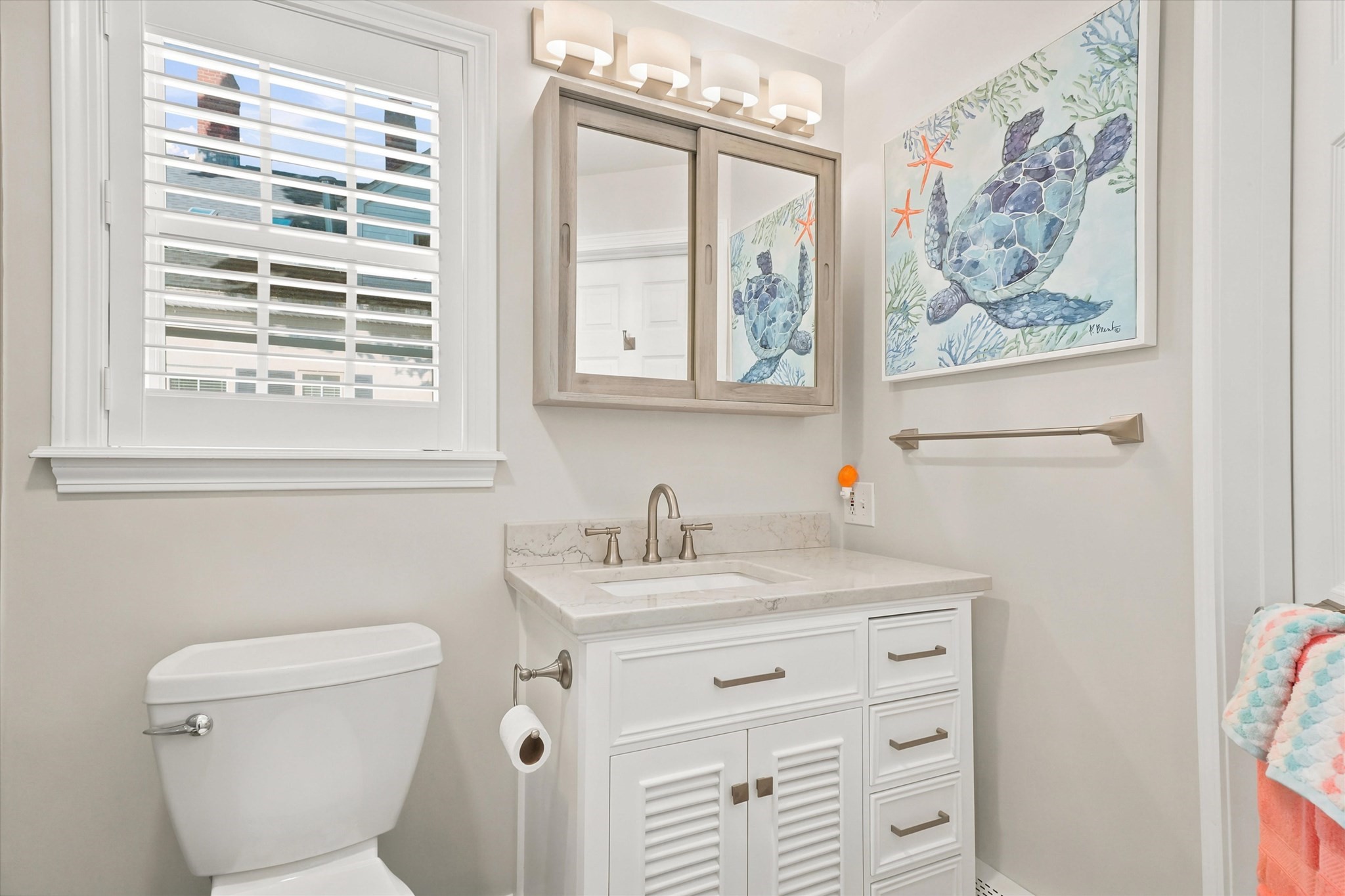 Bright bathroom with a white vanity, marble counter, shuttered window, and sea turtle artwork.