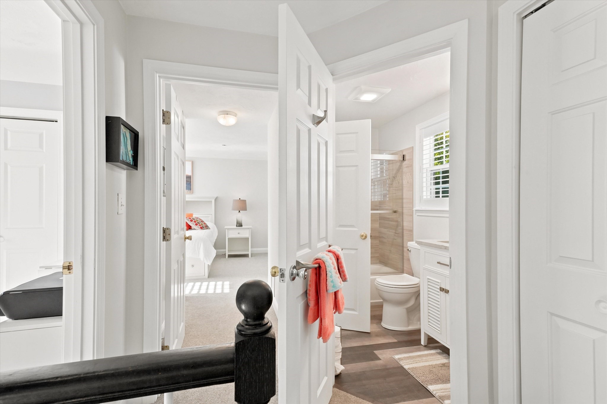 Hallway overlooking a bedroom and bathroom with a tiled shower, white vanity, and coral towels.