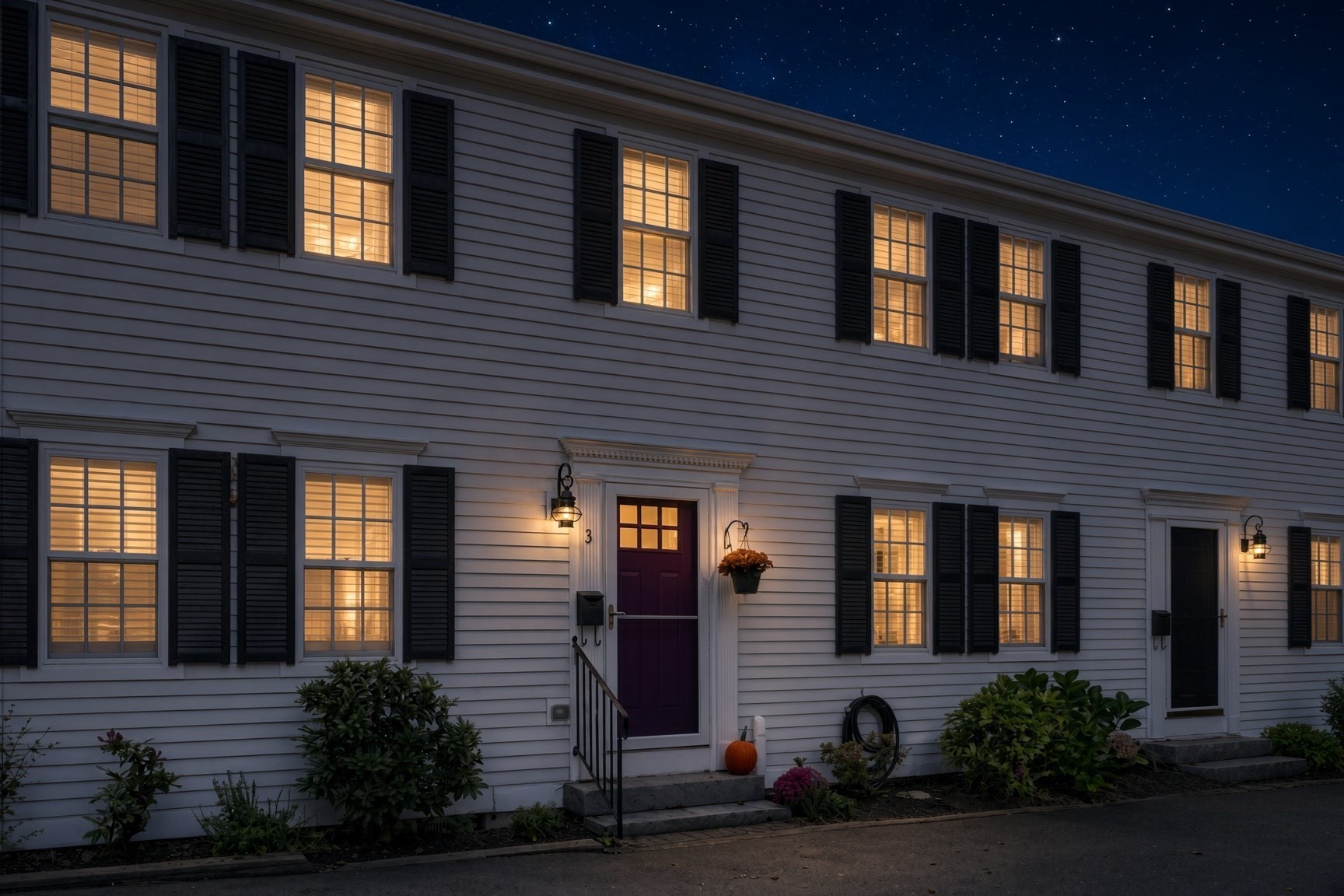 Two-story clapboard building with illuminated windows and a purple entrance door marked 3.