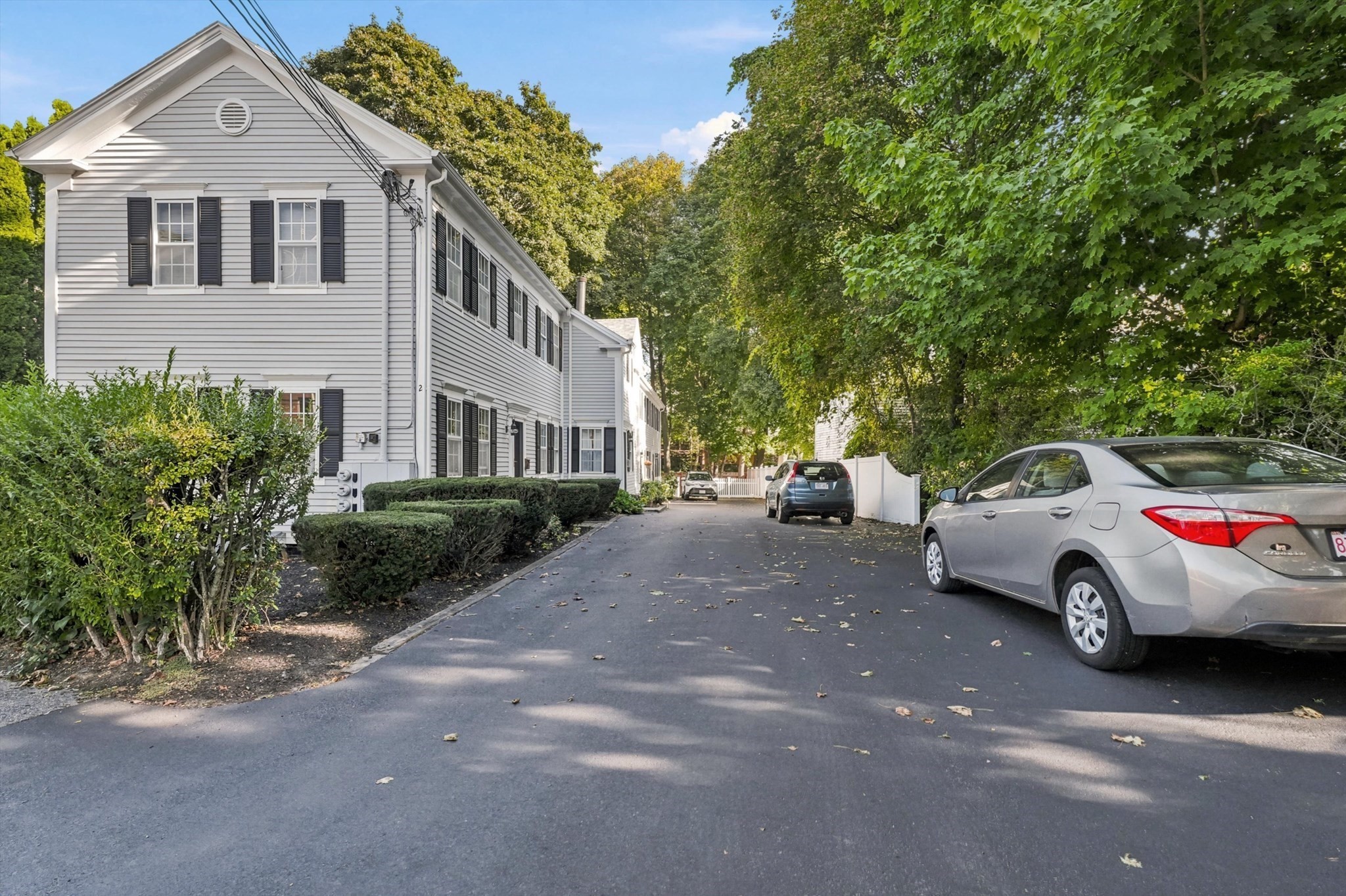 Gray multiunit residence with black shutters beside a paved driveway and mature trees.