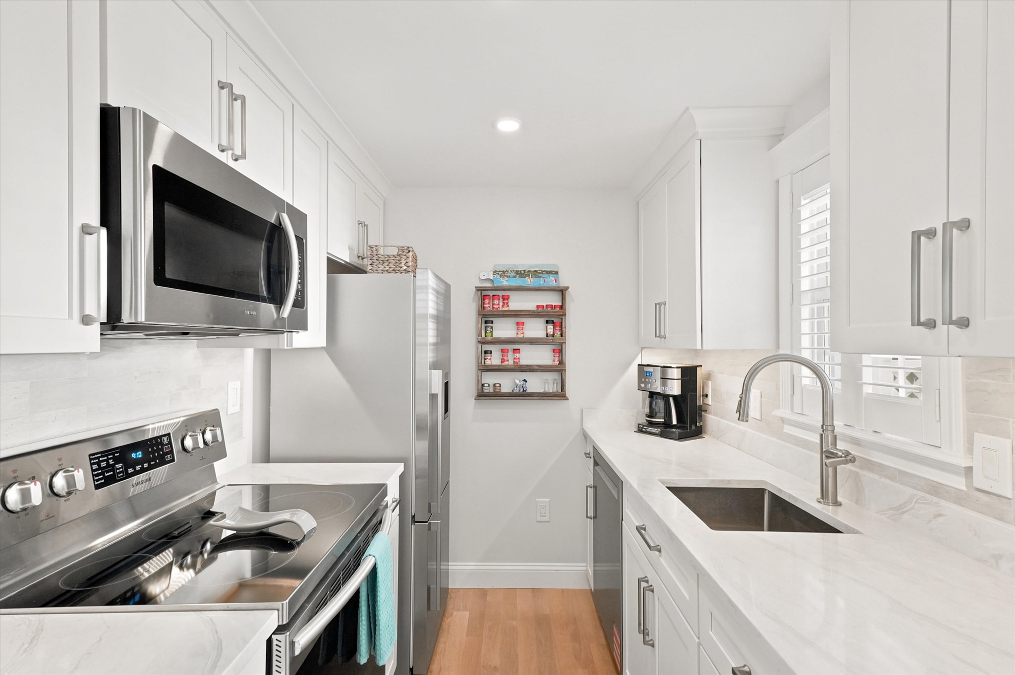 Galley kitchen with white cabinetry, stainless appliances, and a dark sink beneath shuttered windows.