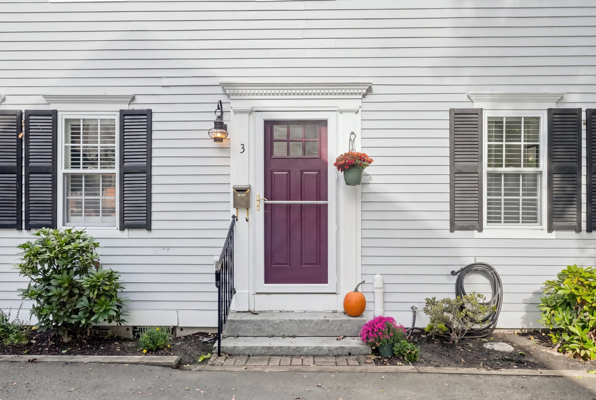 Home entrance with a plum-colored door, black shutters, stone steps, and autumn flowers.