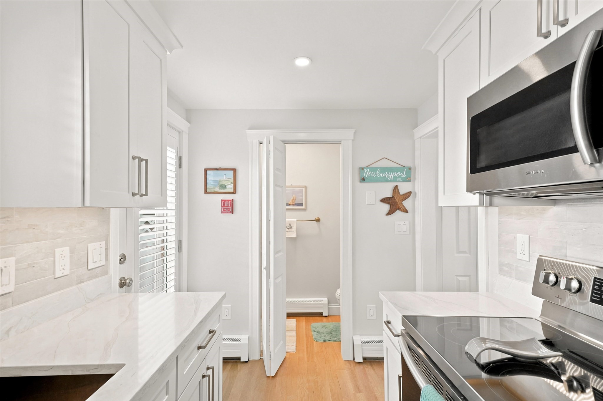 Bright white kitchen with marble-look counters and stainless steel appliances, viewed toward an open bathroom doorway.