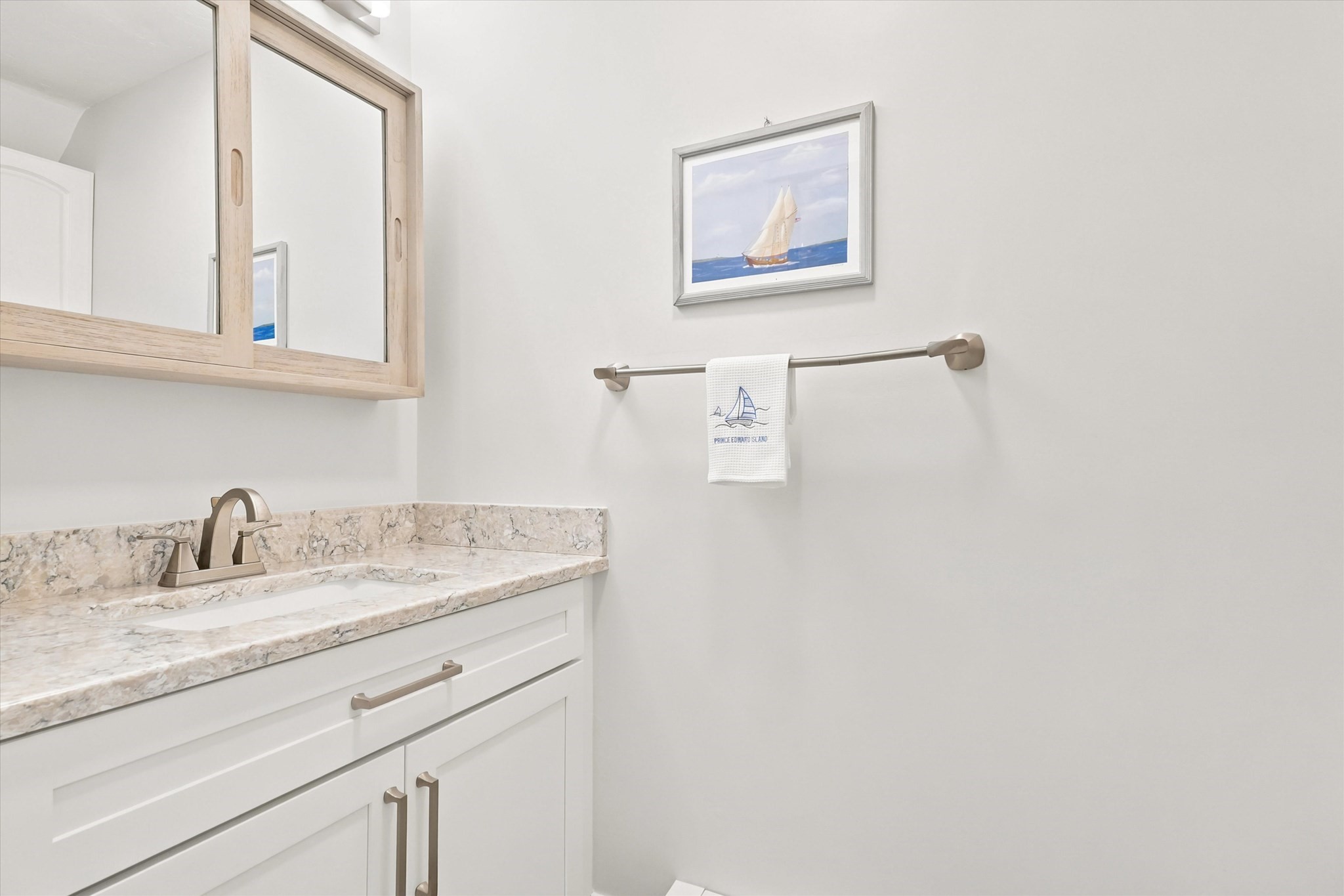 Bathroom vanity with a veined stone counter, light wood-framed mirror, and sailboat towel.
