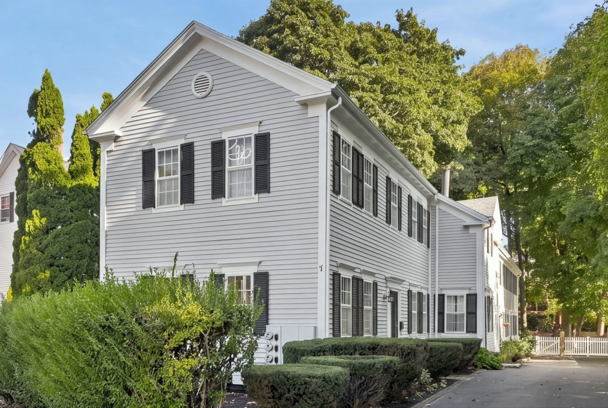 Light-gray residential building with black shutters, landscaped hedges, and a driveway.