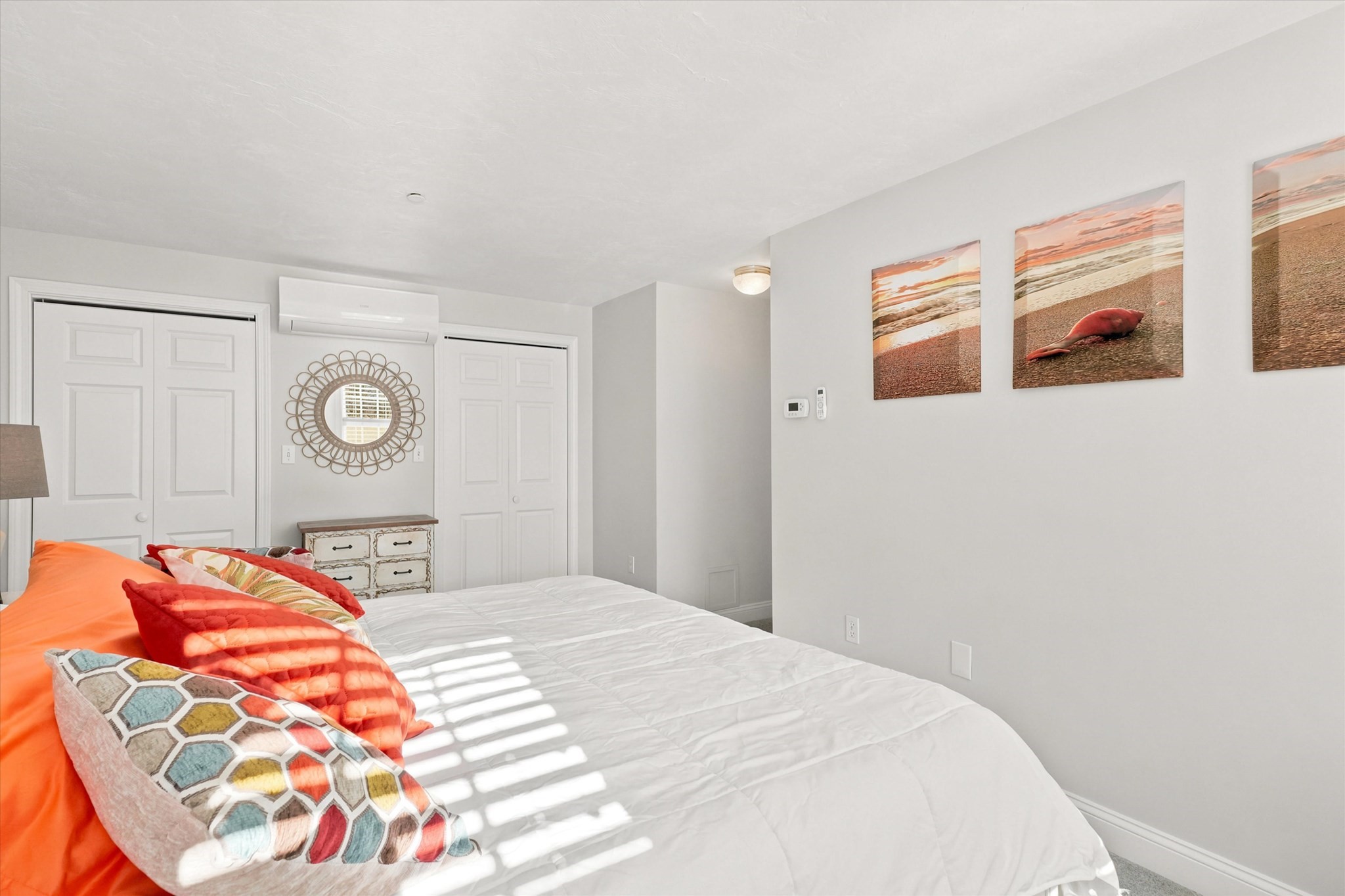 Bright bedroom with a white bed, colorful pillows, and beach-themed wall art.