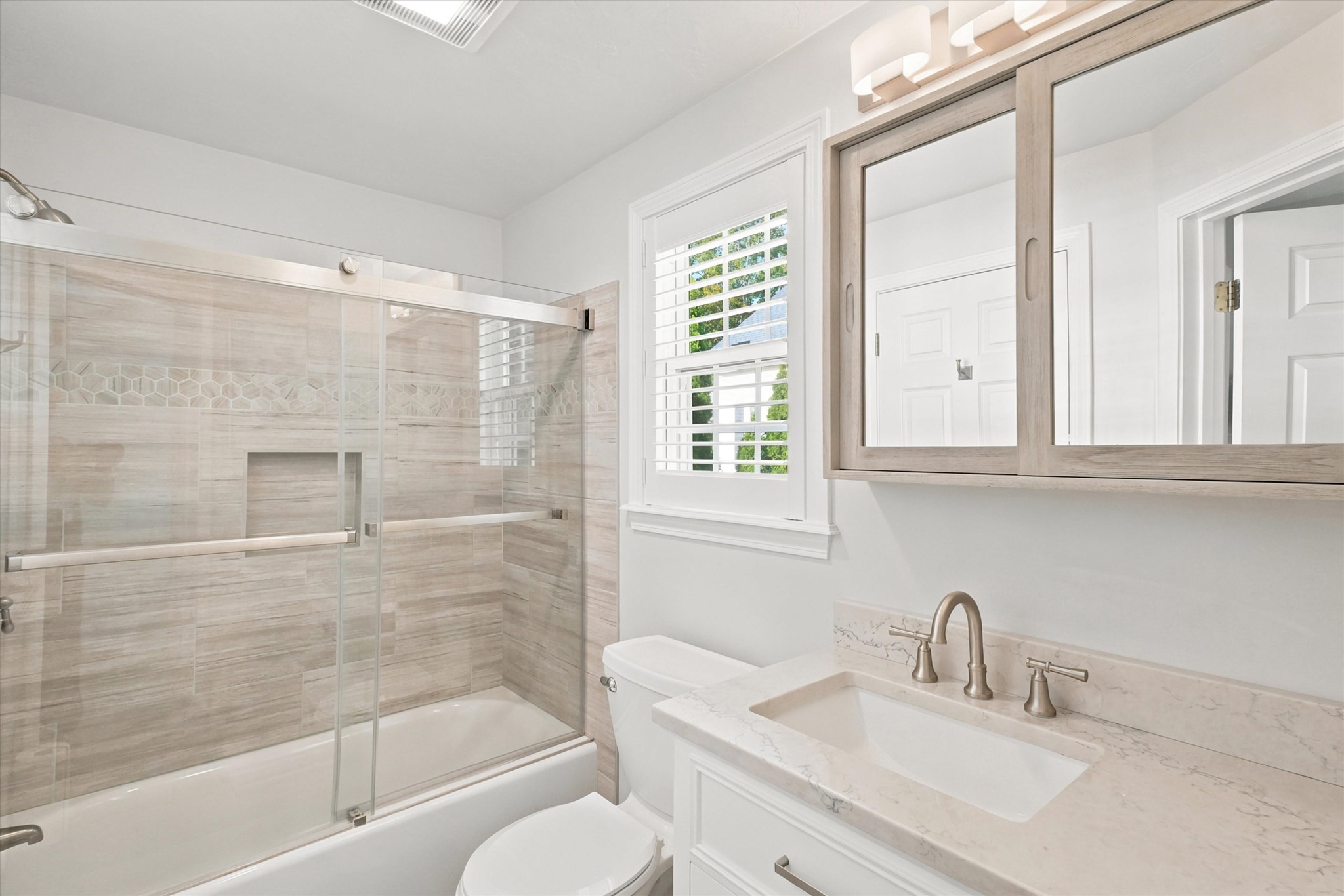 Bathroom with a glass-enclosed tub and shower, mosaic tile band, and white vanity beneath a mirrored cabinet.