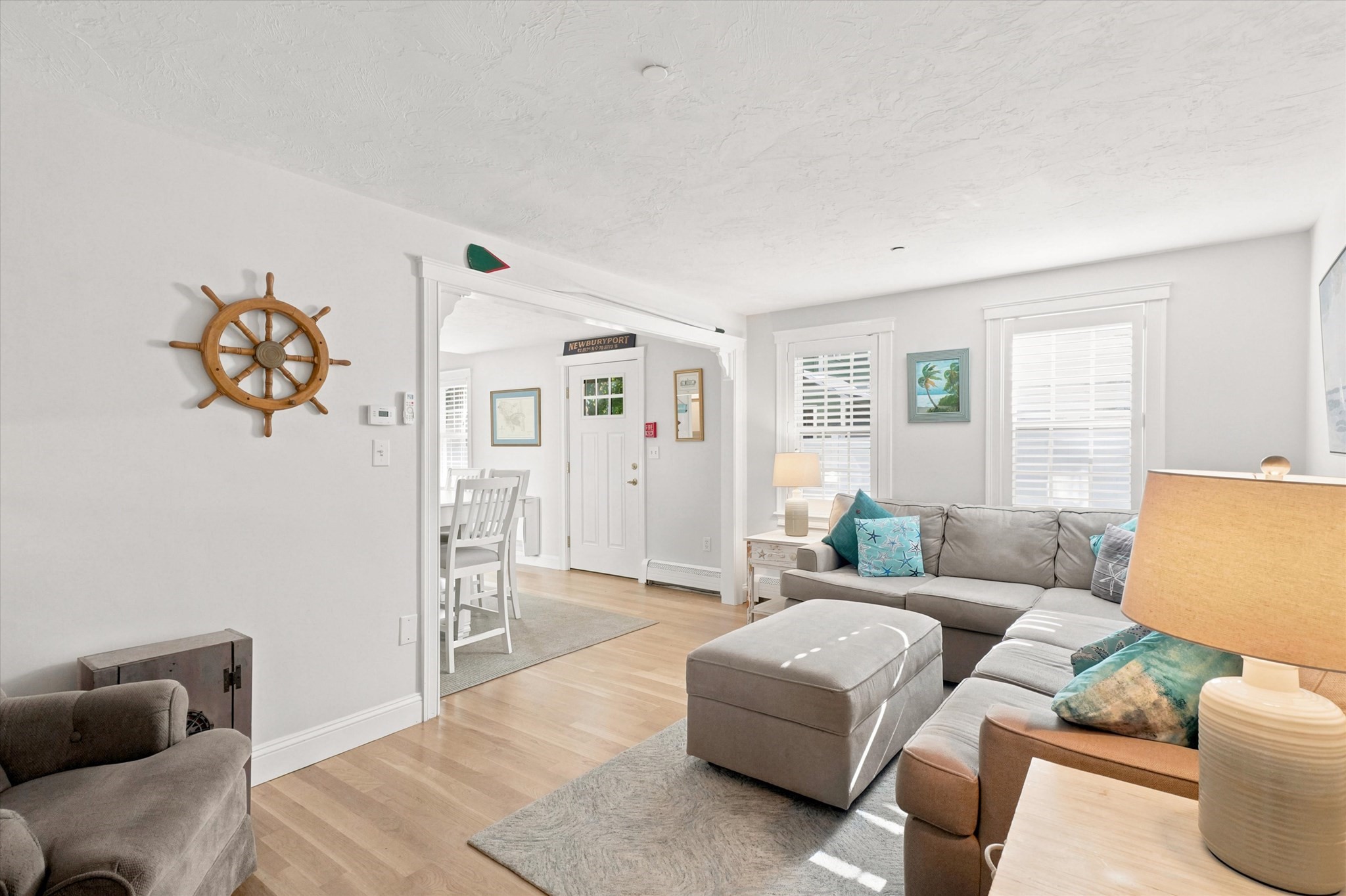 Furnished living room with a gray sectional, light wood floors, and a decorative ship’s wheel.
