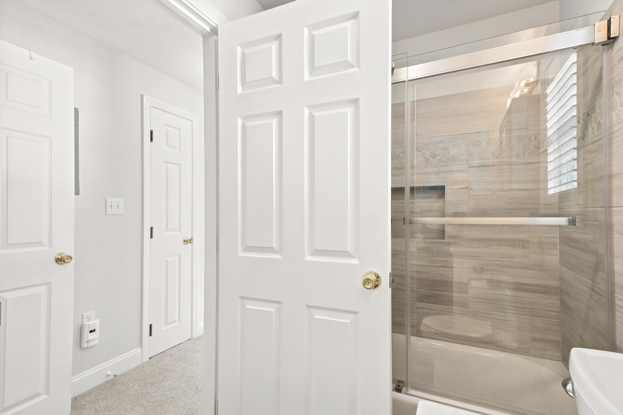 Bathroom shower and tub with beige tile walls and a glass enclosure, viewed past open white doors.