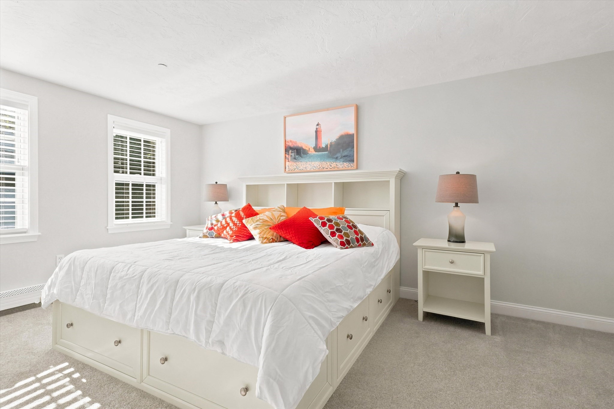 Bright bedroom with a white storage bed, colorful pillows, and framed lighthouse artwork above the headboard.
