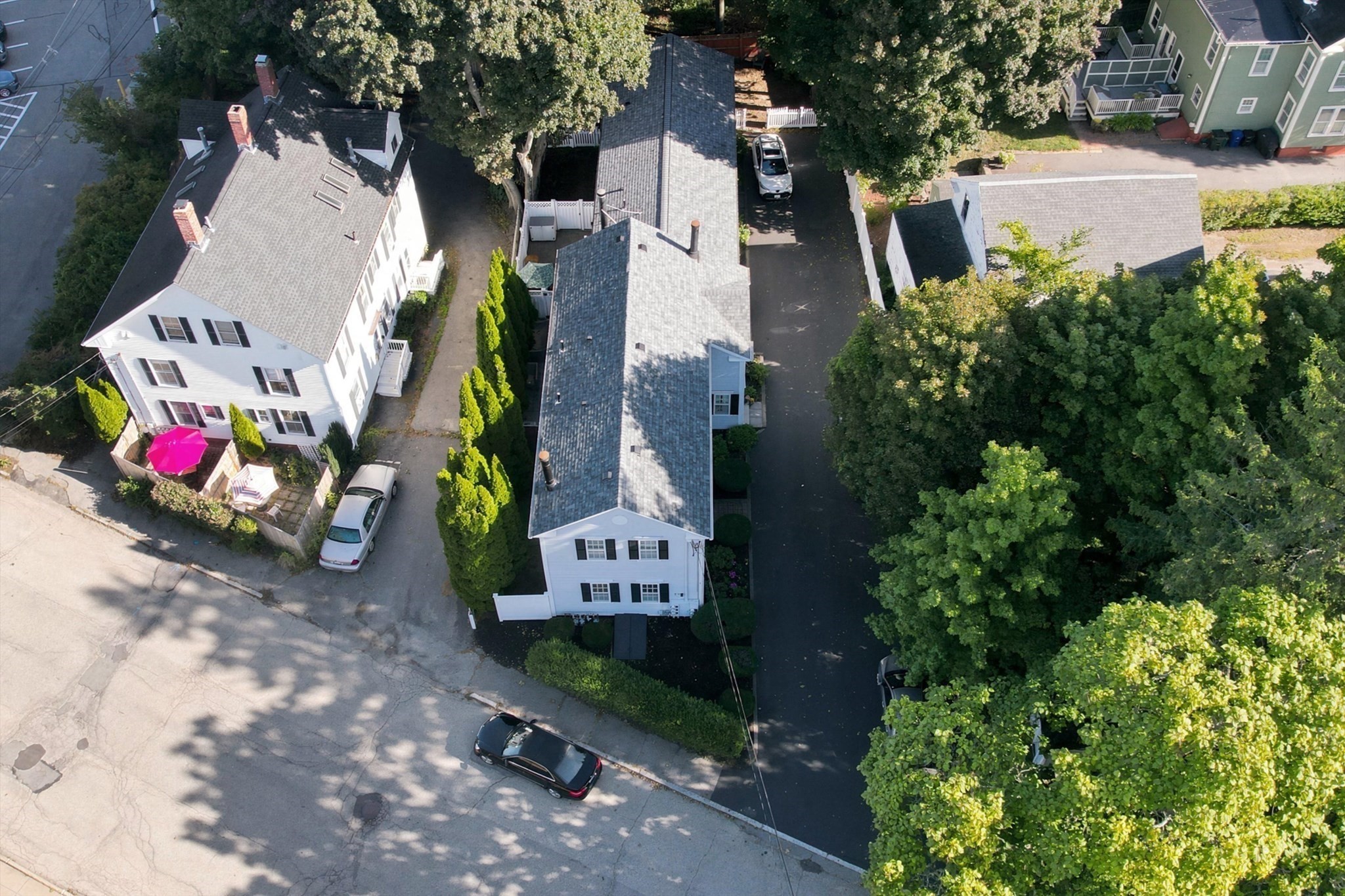 Aerial view of white residential buildings and parking areas shaded by mature trees.
