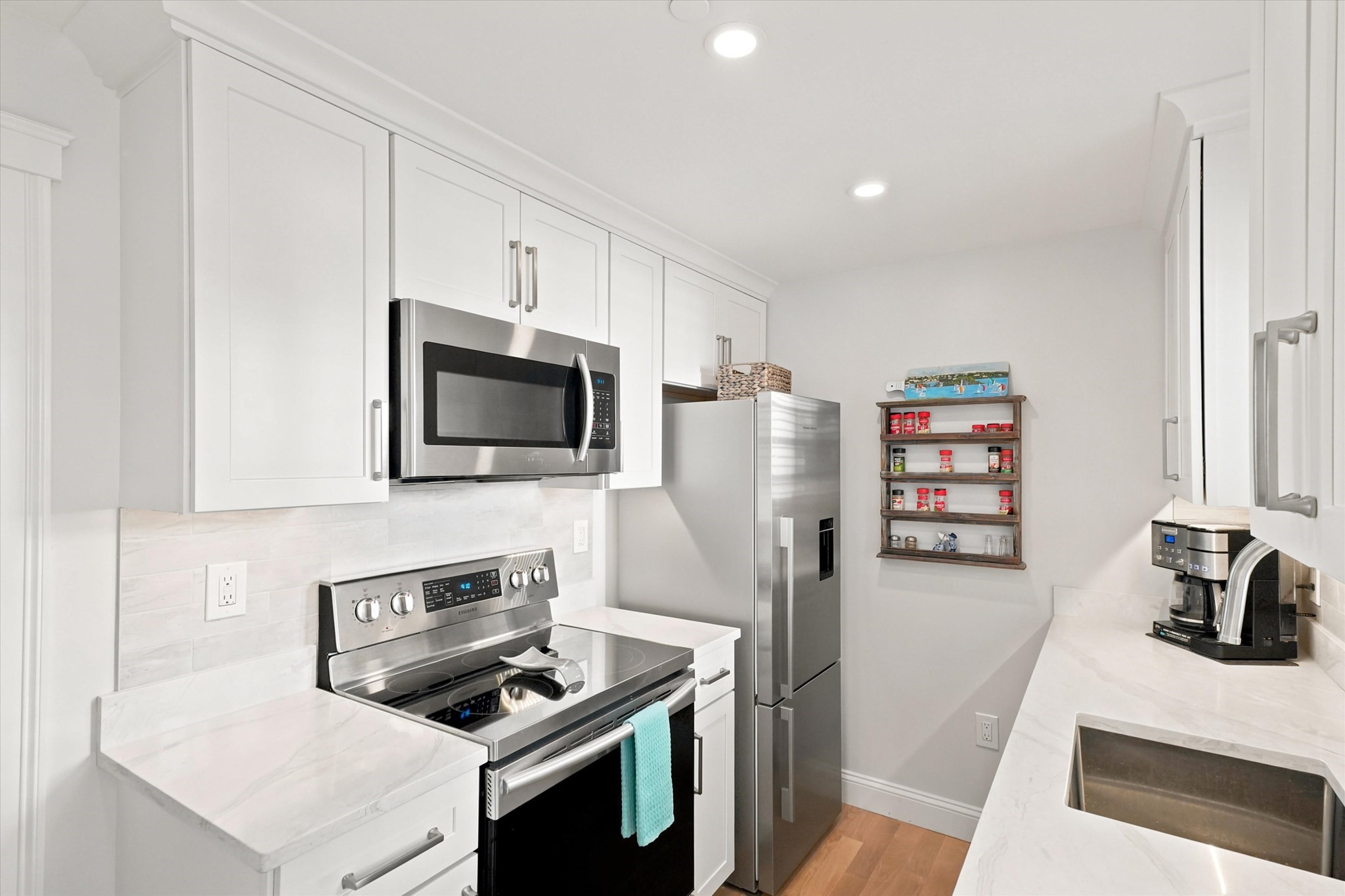 Bright white kitchen with stainless steel appliances, marble-look counters, and a deep farmhouse sink.