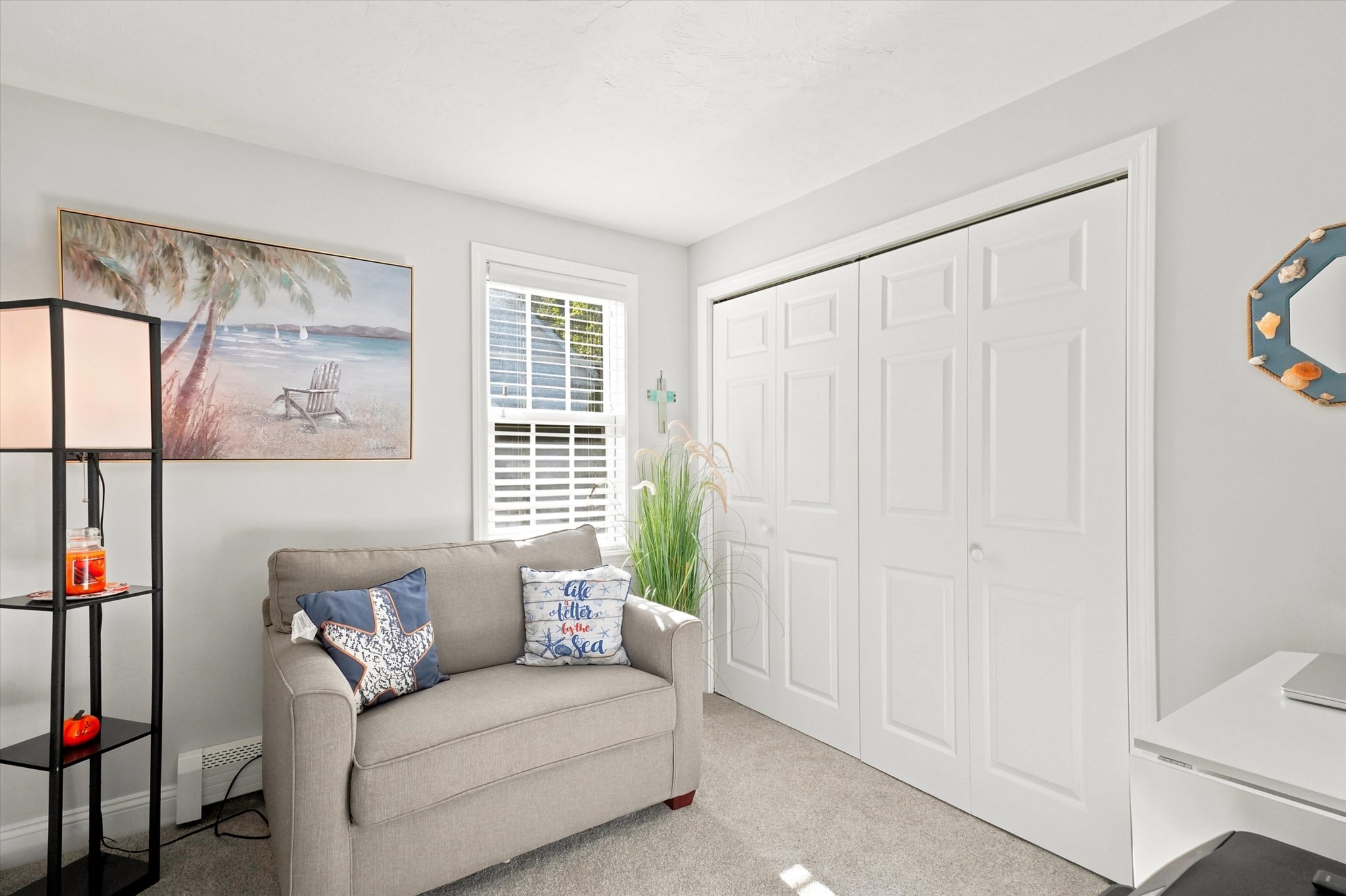 Bright sitting room with a gray loveseat, coastal pillows, beach artwork, and white closet doors.