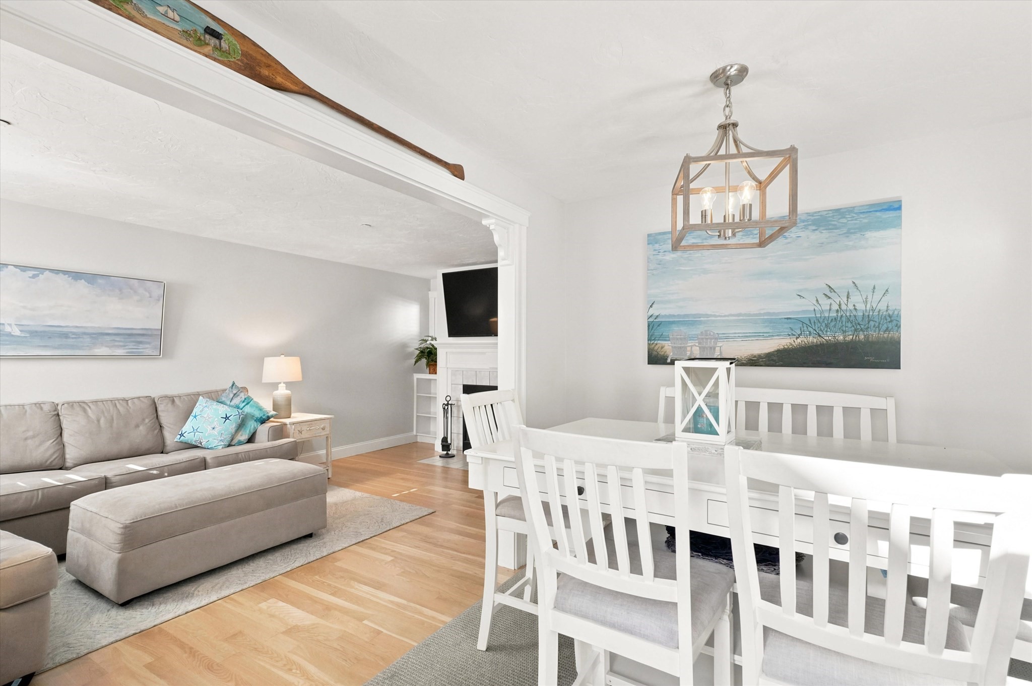 Open-plan living and dining room with a gray sectional, white dining set, and coastal artwork.