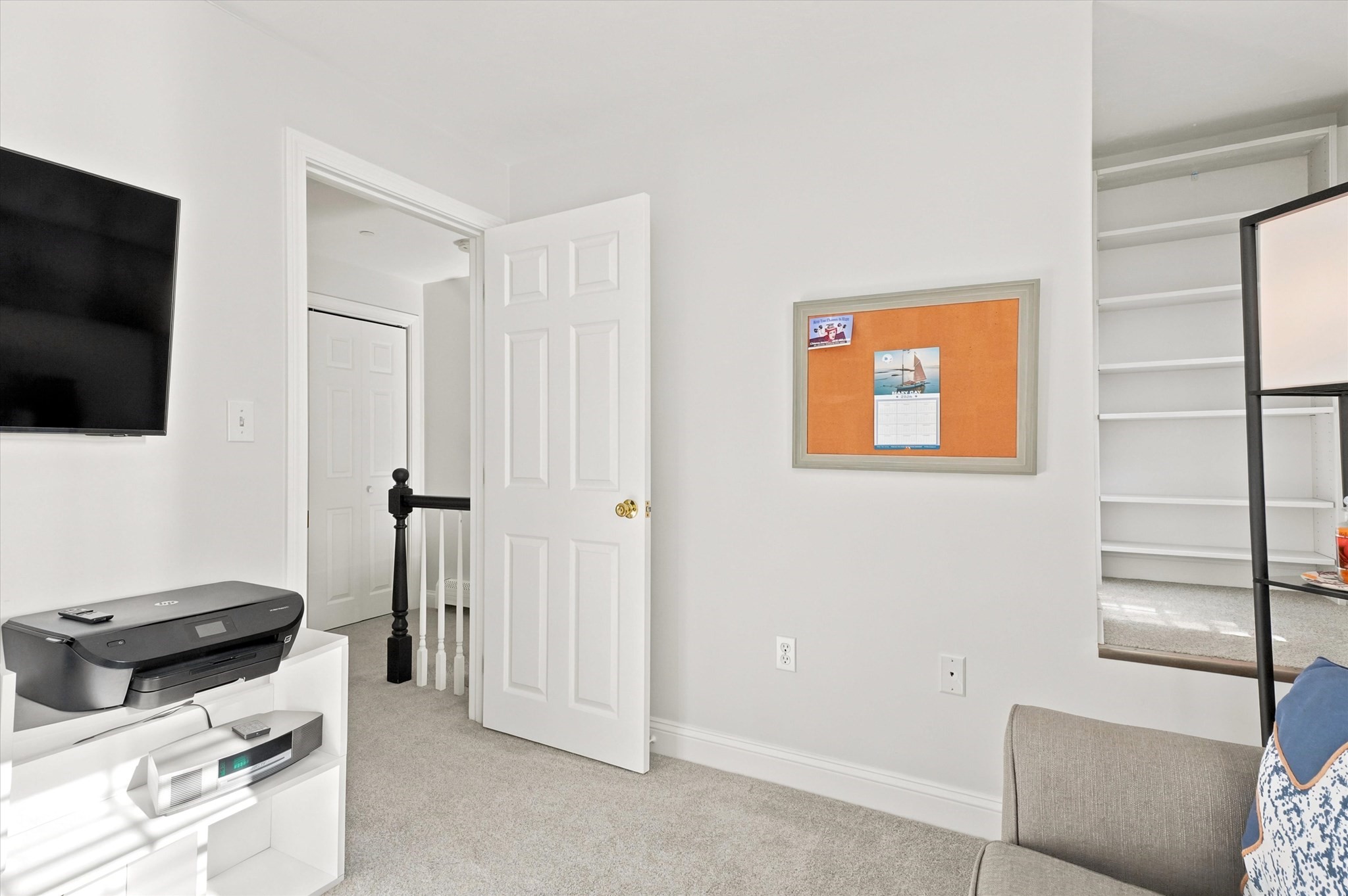 Carpeted room with a wall-mounted TV, printer, open door, and built-in shelves.