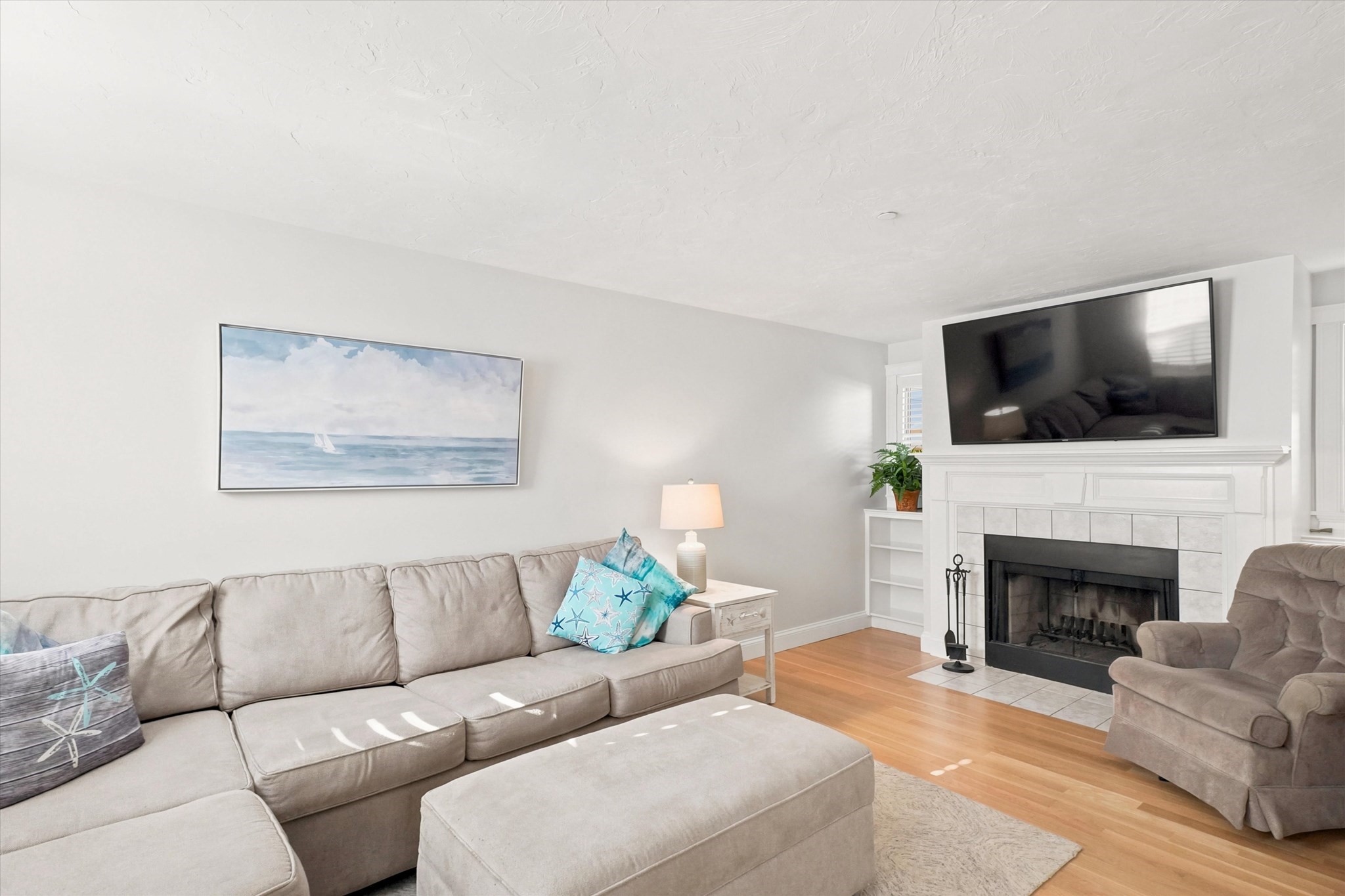Furnished living room with a white fireplace, wall-mounted television, and light sectional sofa.