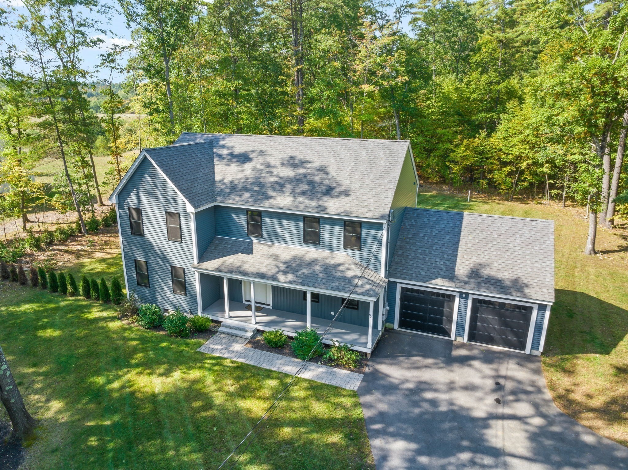 Blue two-story house with a covered porch, attached two-car garage, and wooded yard.
