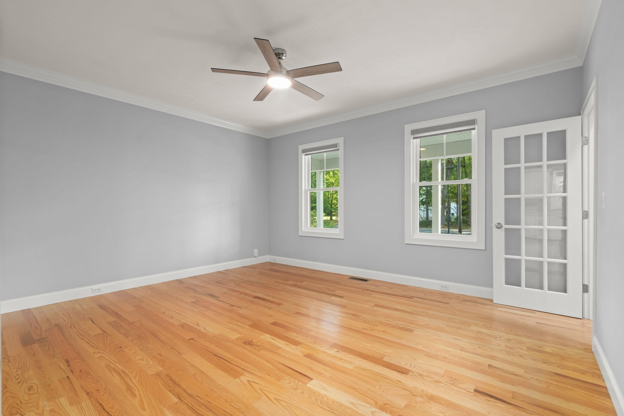 Empty room with hardwood floors, gray walls, two windows, and a ceiling fan.