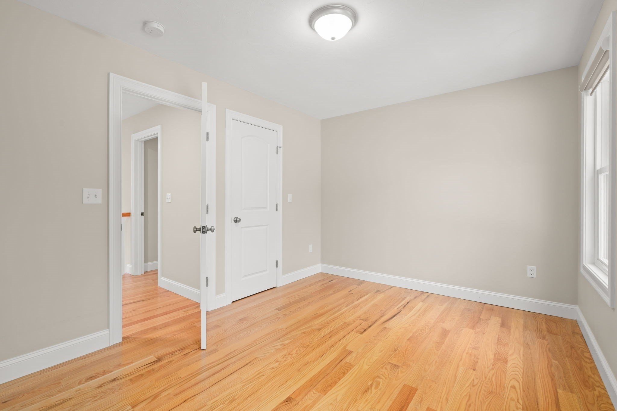 Empty room with hardwood floors, beige walls, and a window.