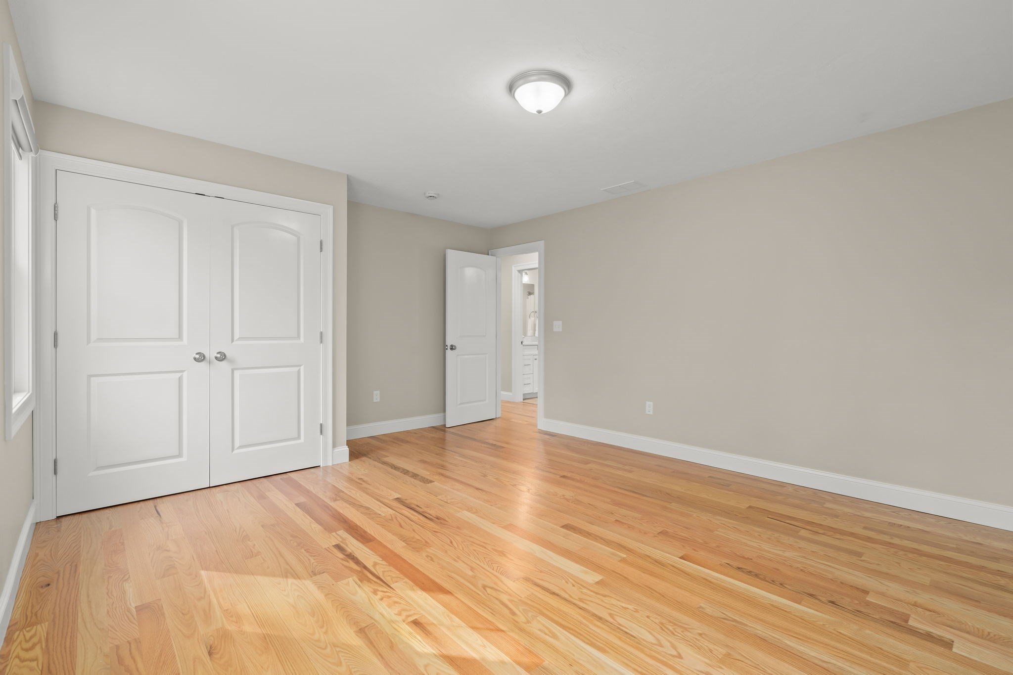 Empty room with light hardwood floors, double closet doors, and an open bathroom doorway.