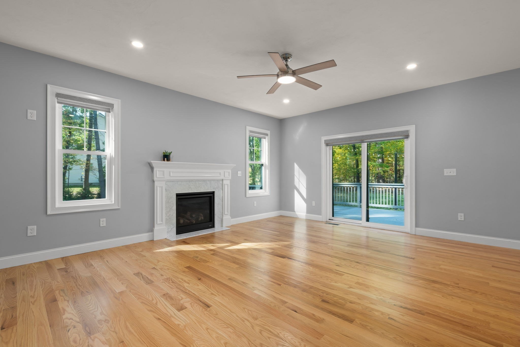 Empty living room with hardwood floors, a white fireplace, and sliding doors to a deck.
