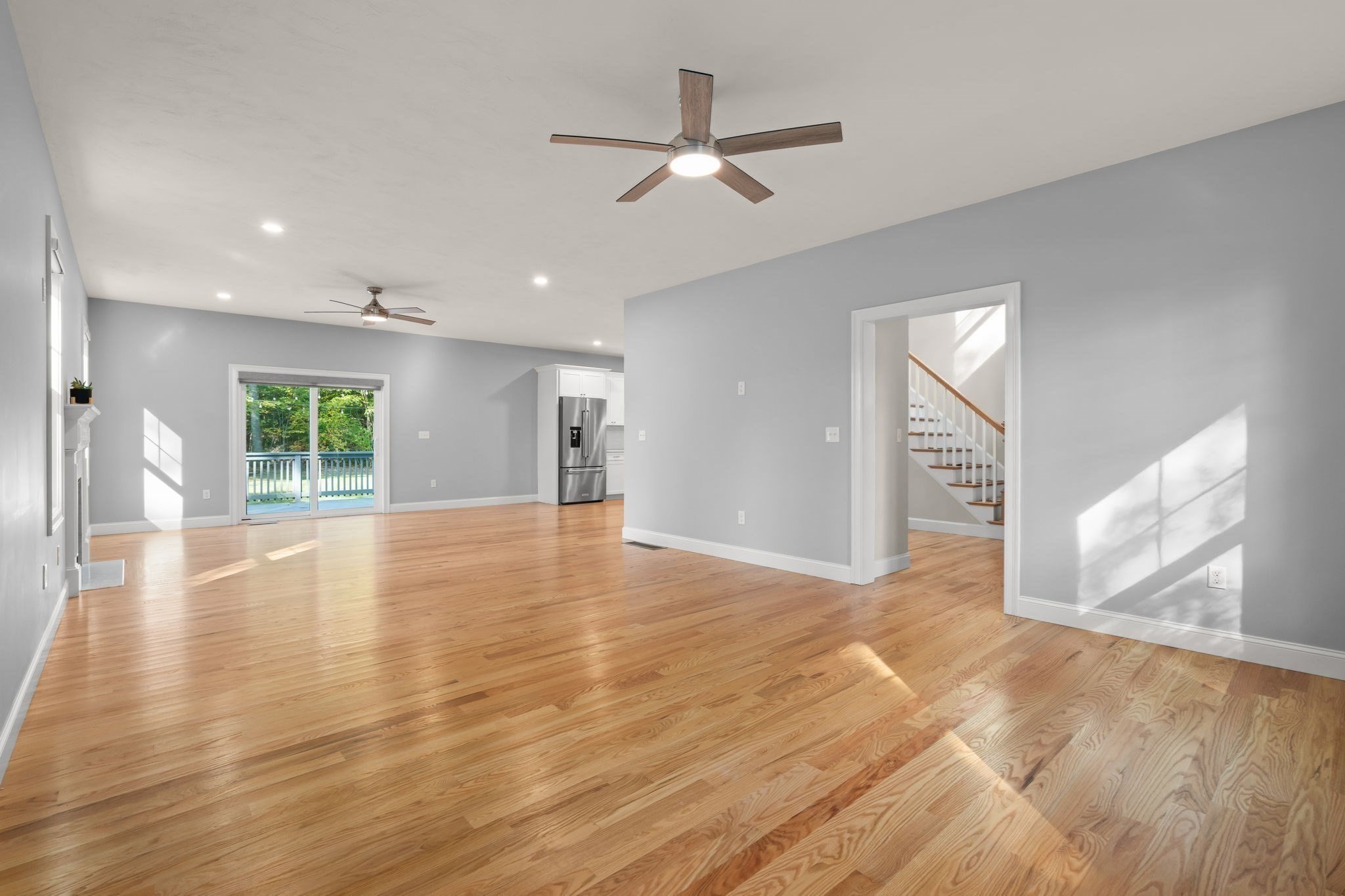 Unfurnished living area with hardwood floors, sliding deck doors, and a staircase.