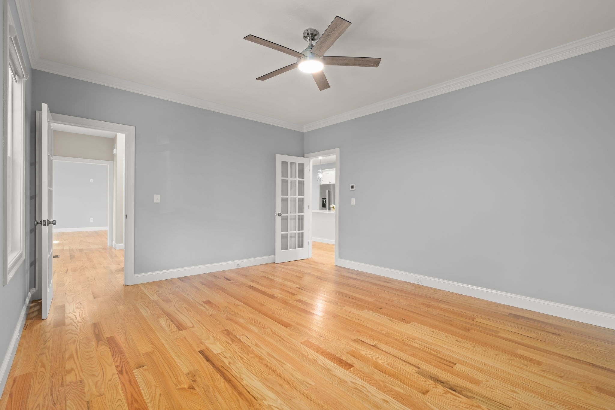 Empty room with gray walls, hardwood floors, and a ceiling fan with light.