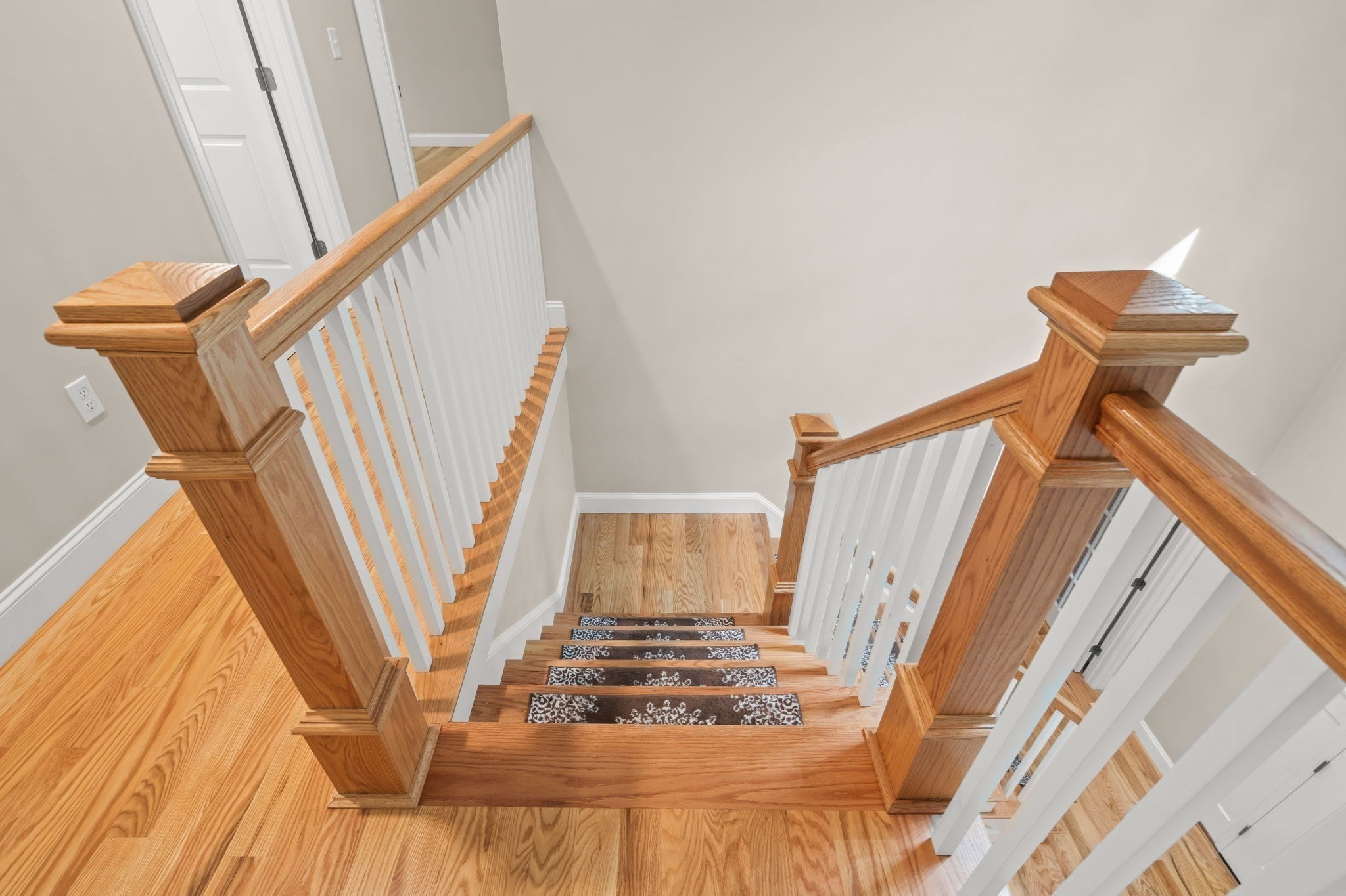 Hardwood staircase with patterned tread runners, white balusters, and polished wood handrails.