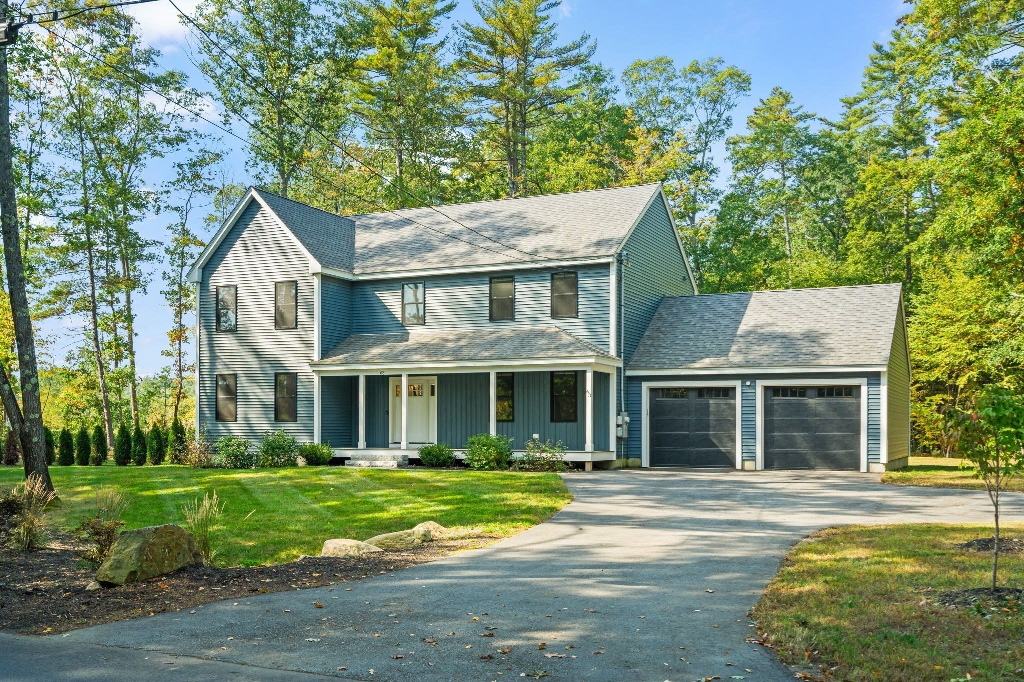 Blue-gray two-story home with a covered porch, attached two-car garage, and tree-lined lawn.