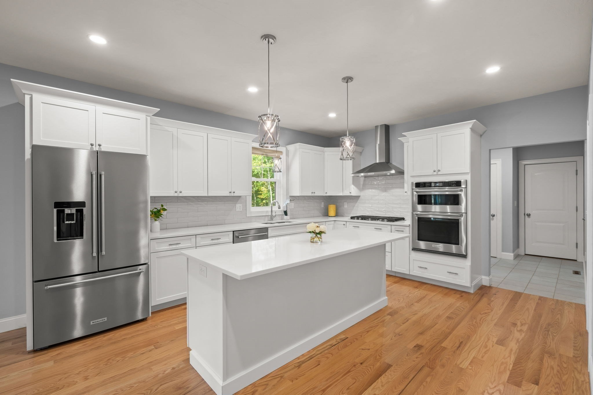 Renovated kitchen with a large white island, stainless steel appliances, and hardwood floors.
