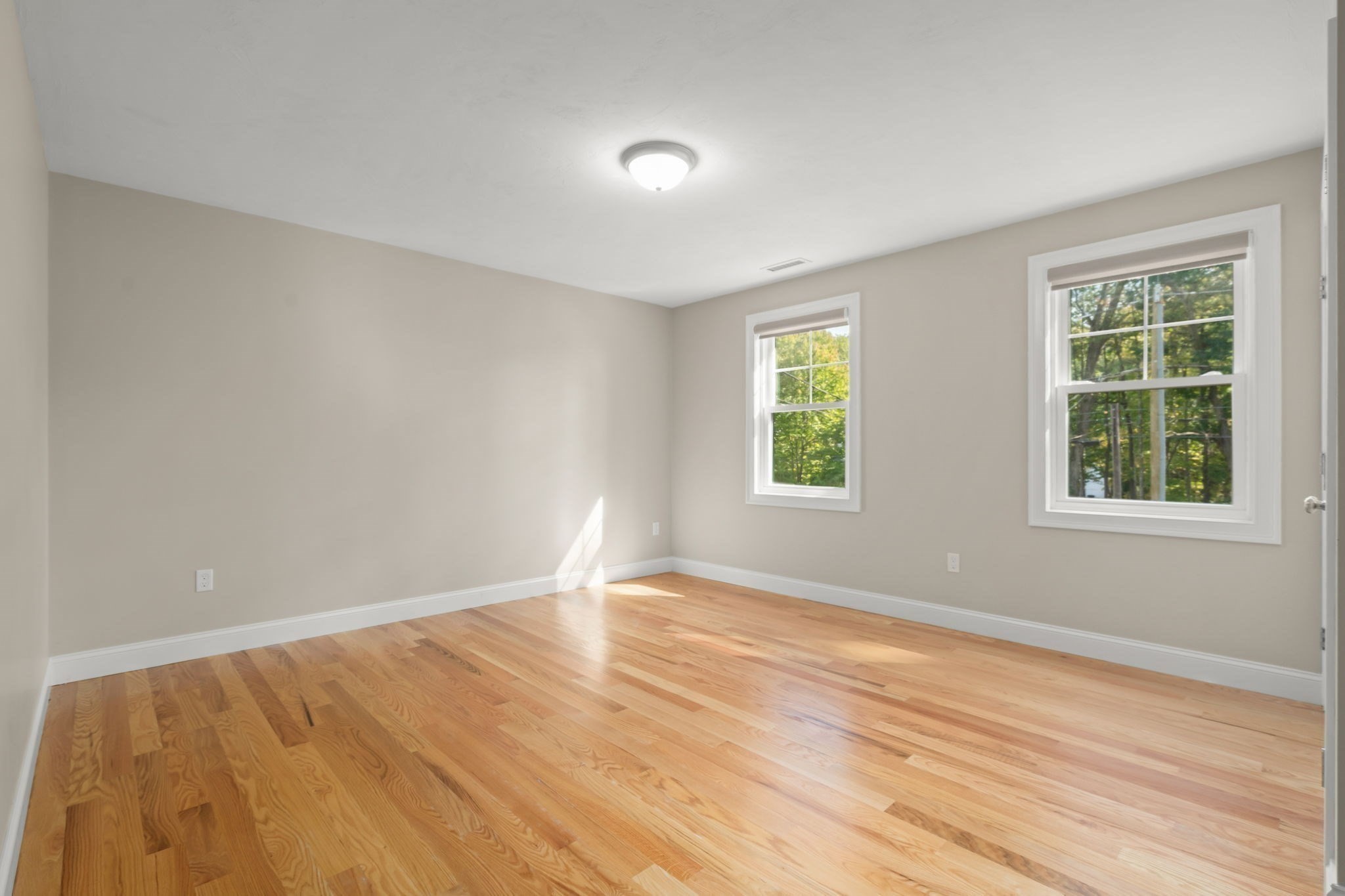 Empty room with polished hardwood floors and two windows letting in sunlight.