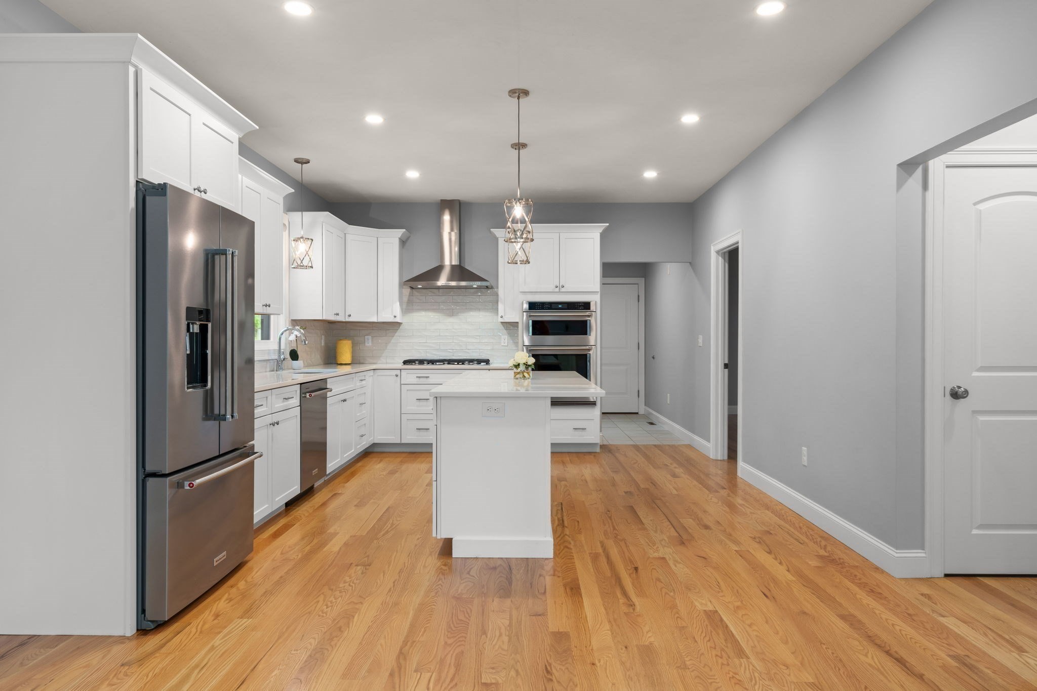Renovated kitchen with white cabinets, stainless steel appliances, central island, and warm hardwood floors.