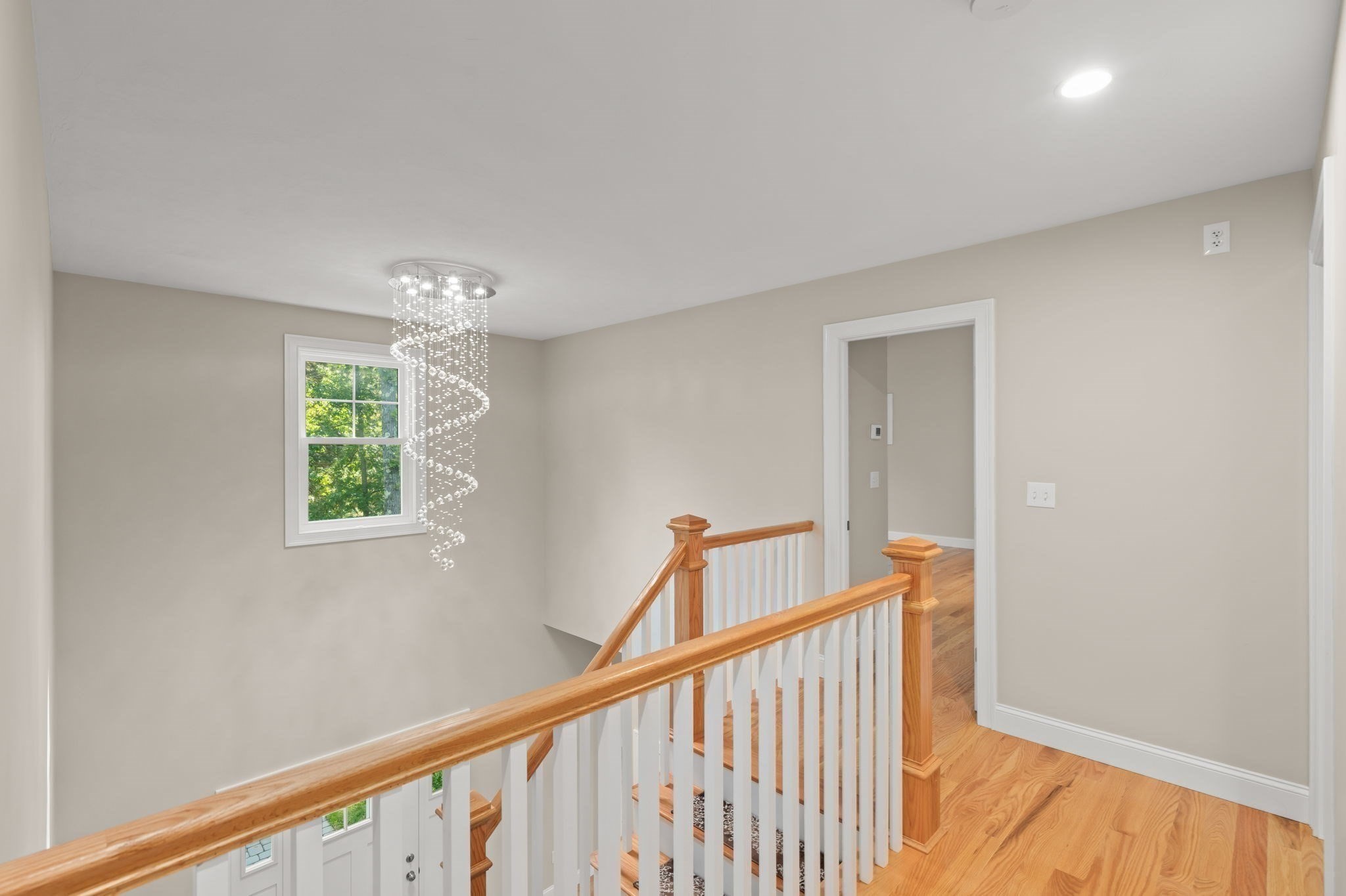 Upstairs landing with a crystal chandelier, hardwood floors, and a wood-and-white stair railing.