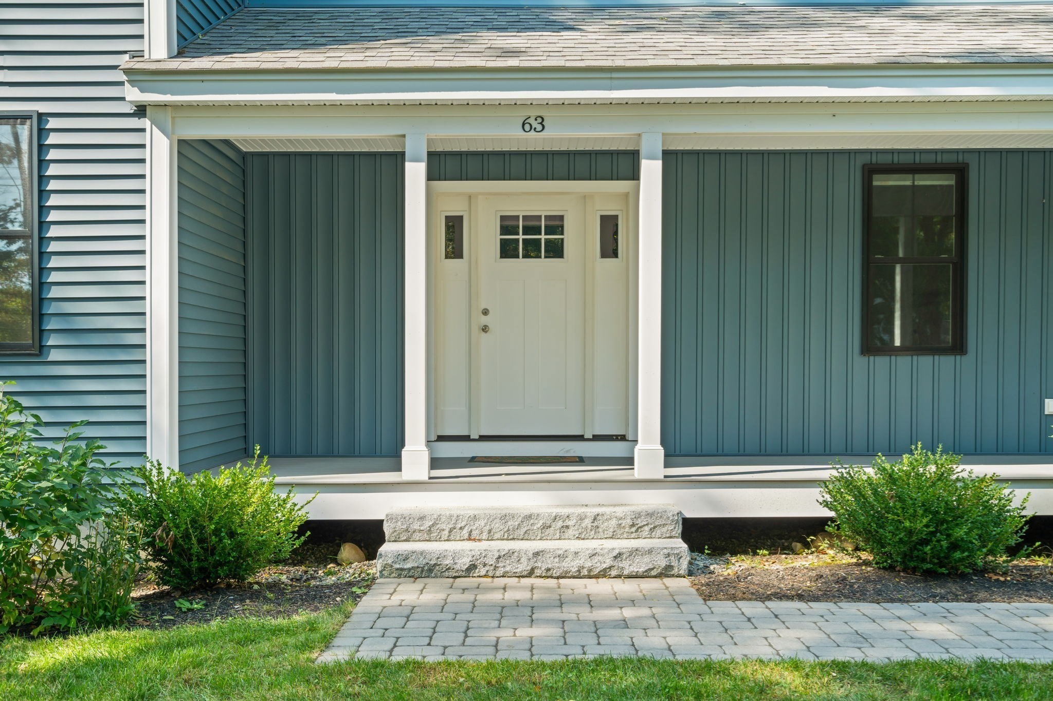 Front entrance of a blue-gray house with white door, stone steps, and a paver walkway.