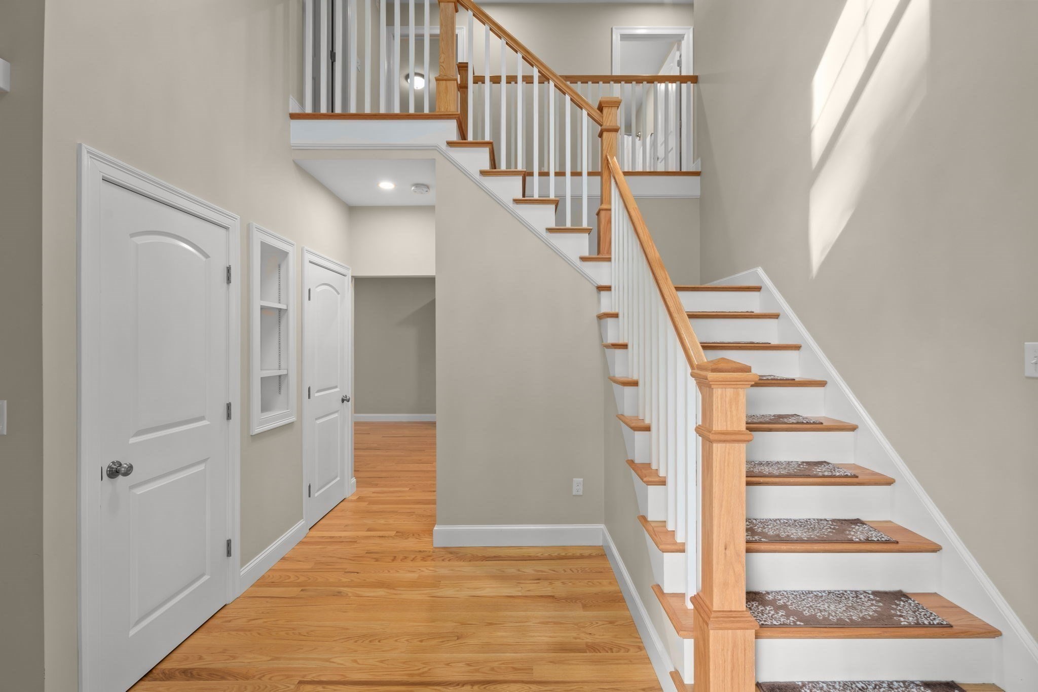 Foyer with a wood-and-white staircase, patterned runners, and hardwood floors.