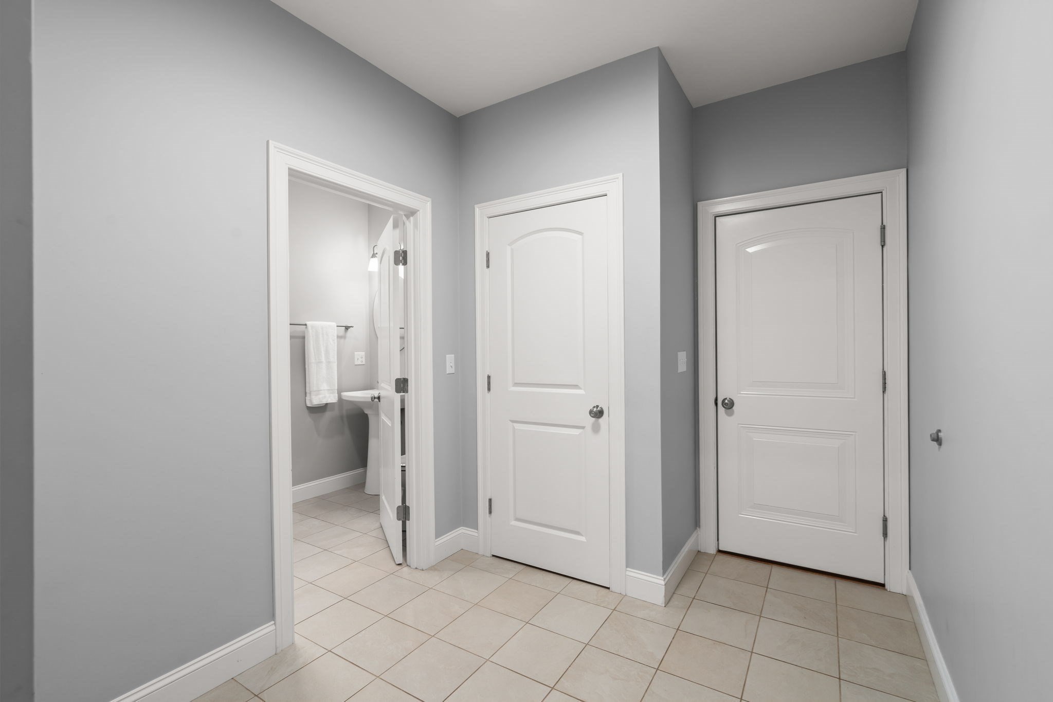 Hallway with tiled floor, two white doors, and an open doorway to a bathroom.