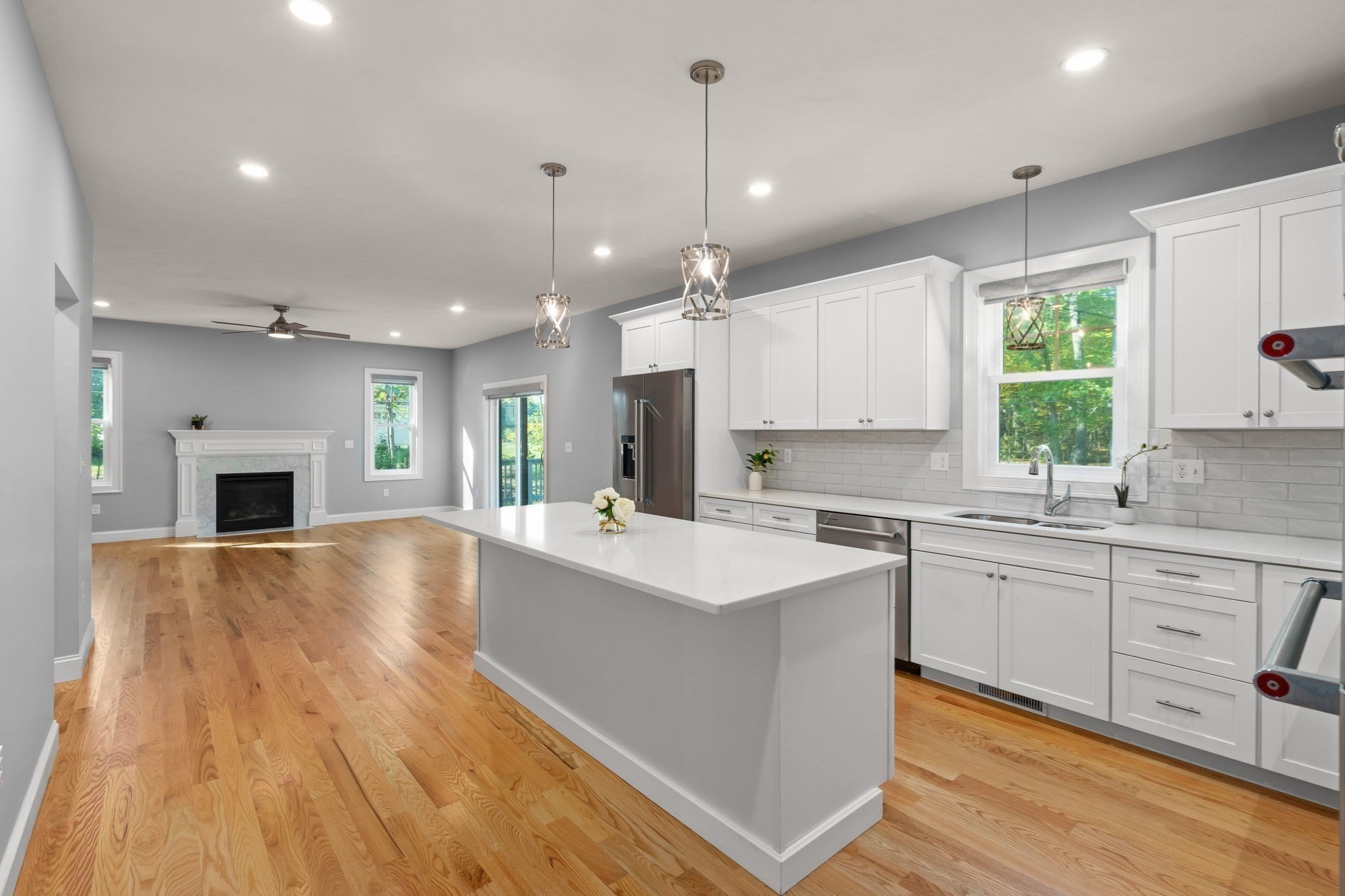 Open kitchen with a large white island and hardwood floors, adjoining a living area with a fireplace.