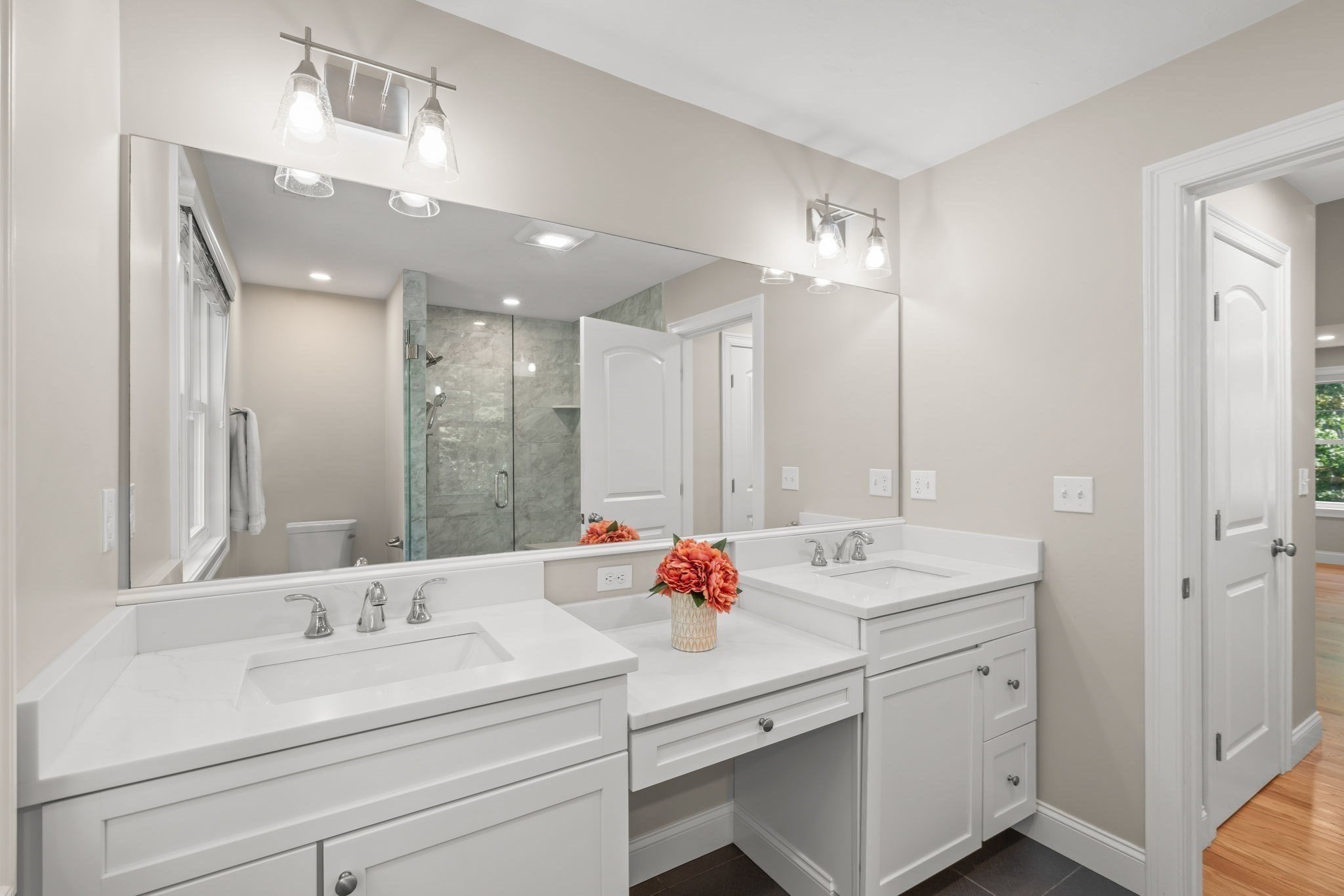 Bathroom with double white vanities, a wide mirror, and a glass-enclosed gray-tile shower.