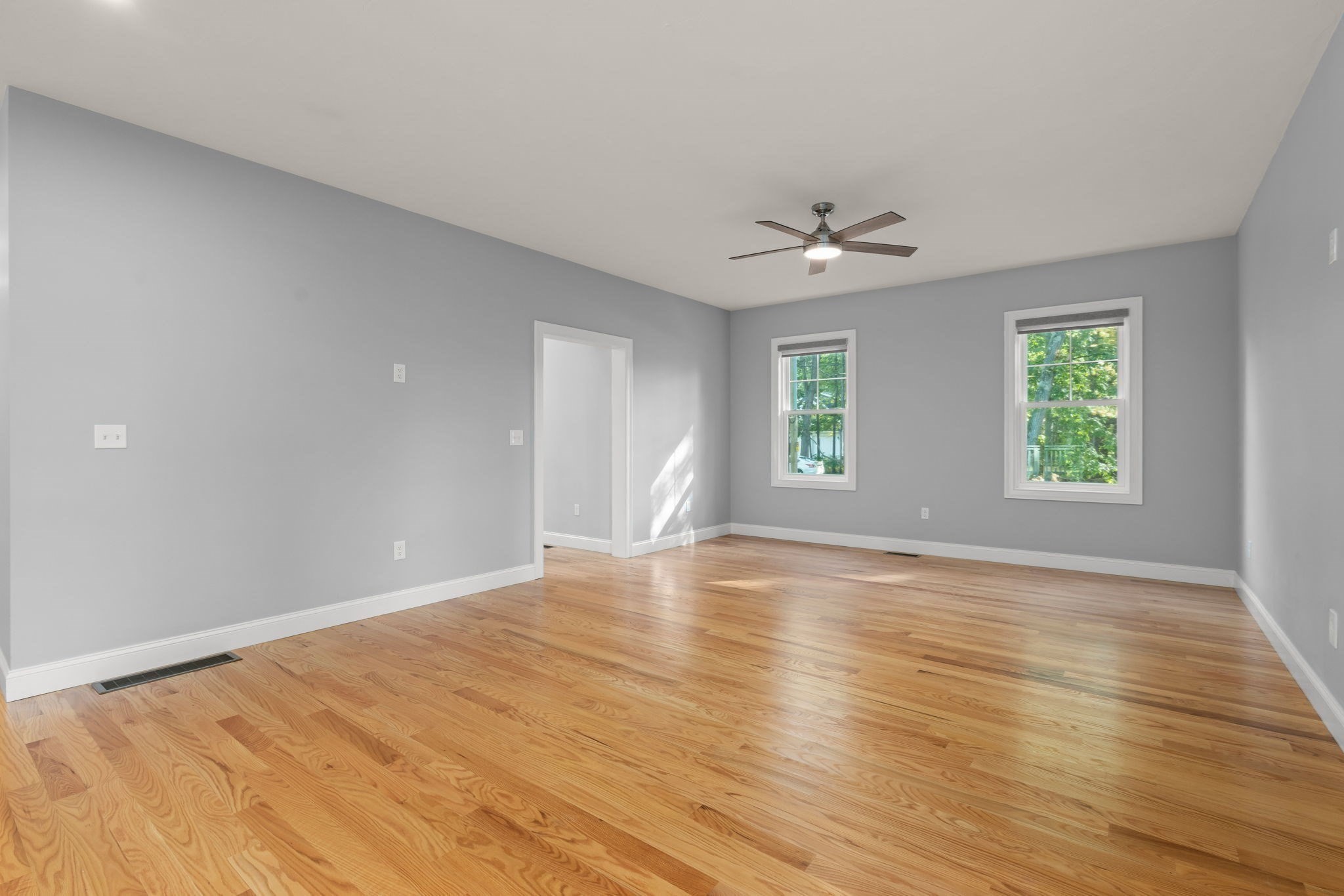 Vacant room with polished hardwood floors, gray walls, and two windows.