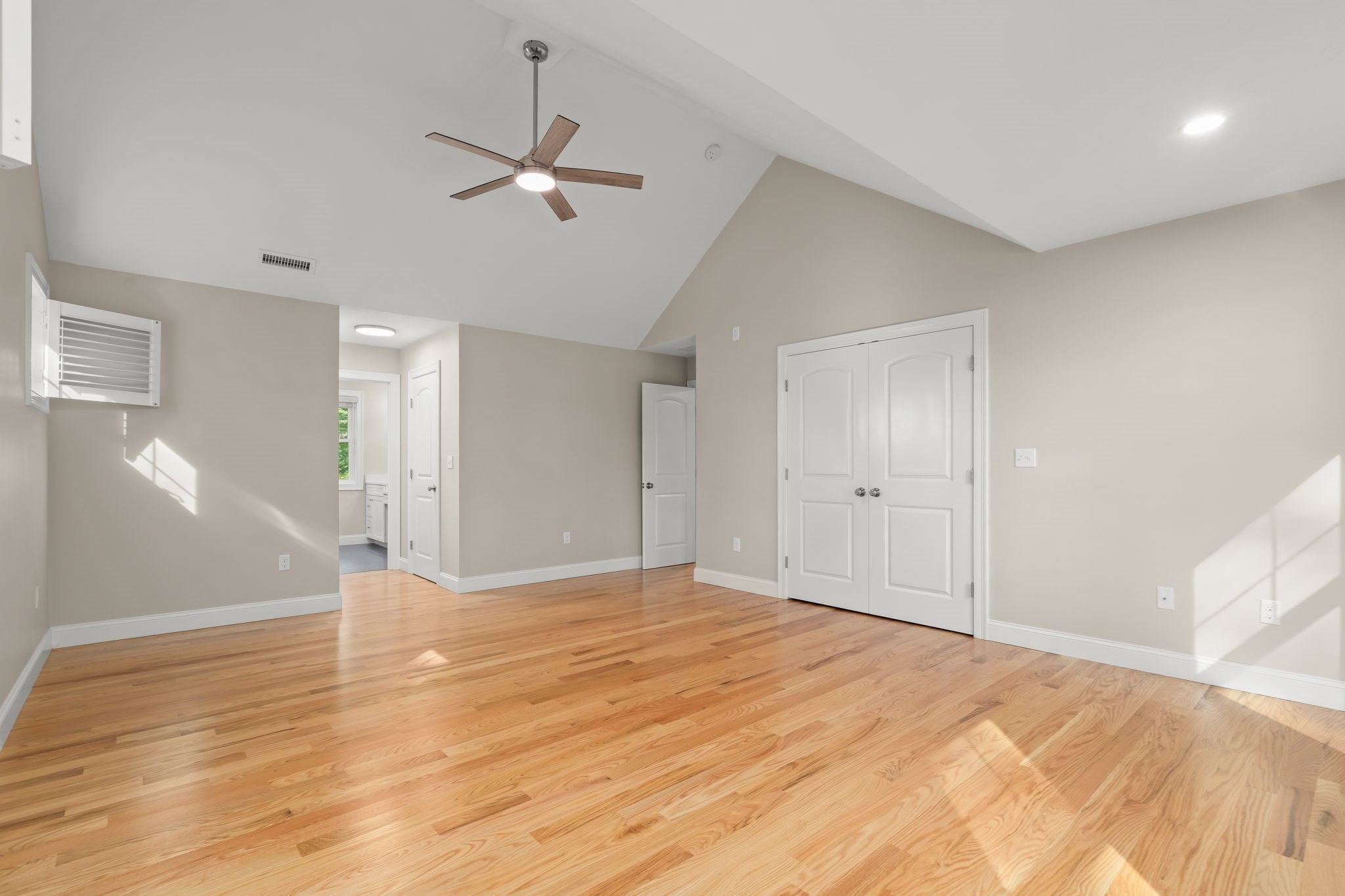 Vacant room with hardwood floors, a vaulted ceiling, and white double closet doors.