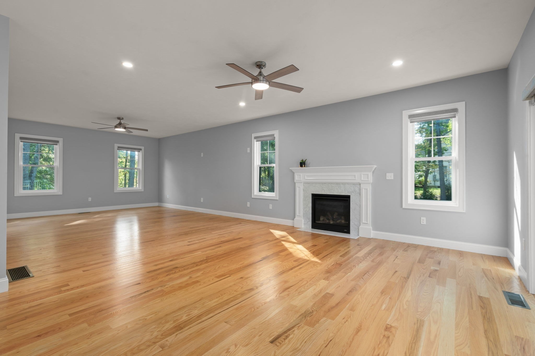 Vacant living room with hardwood floors, gray walls, and a white fireplace mantel.