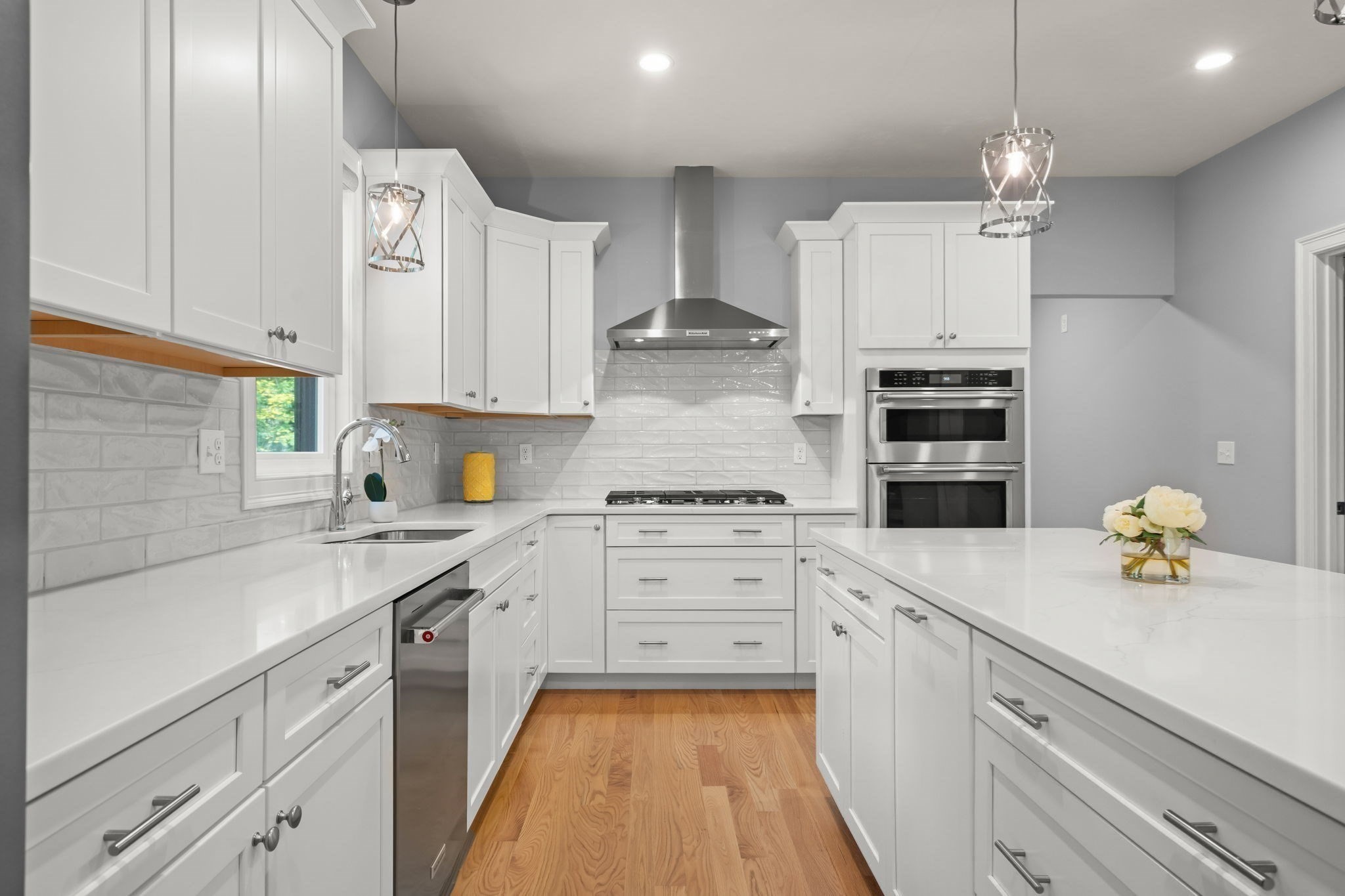 Kitchen with white cabinets, a large island, stainless steel double ovens, and warm wood floors.