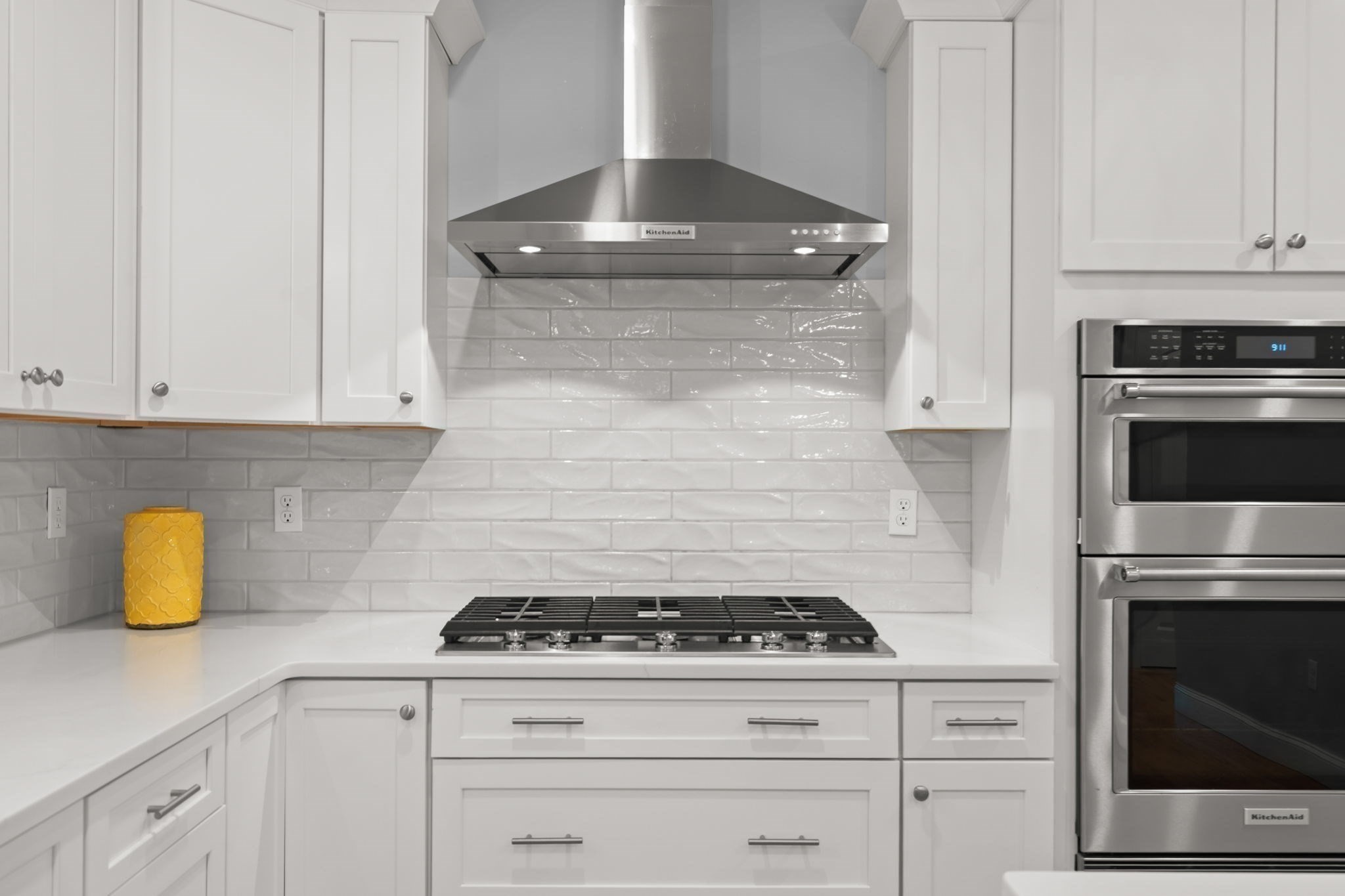 White kitchen with subway tile backsplash, gas cooktop, stainless steel hood, and built-in double oven.