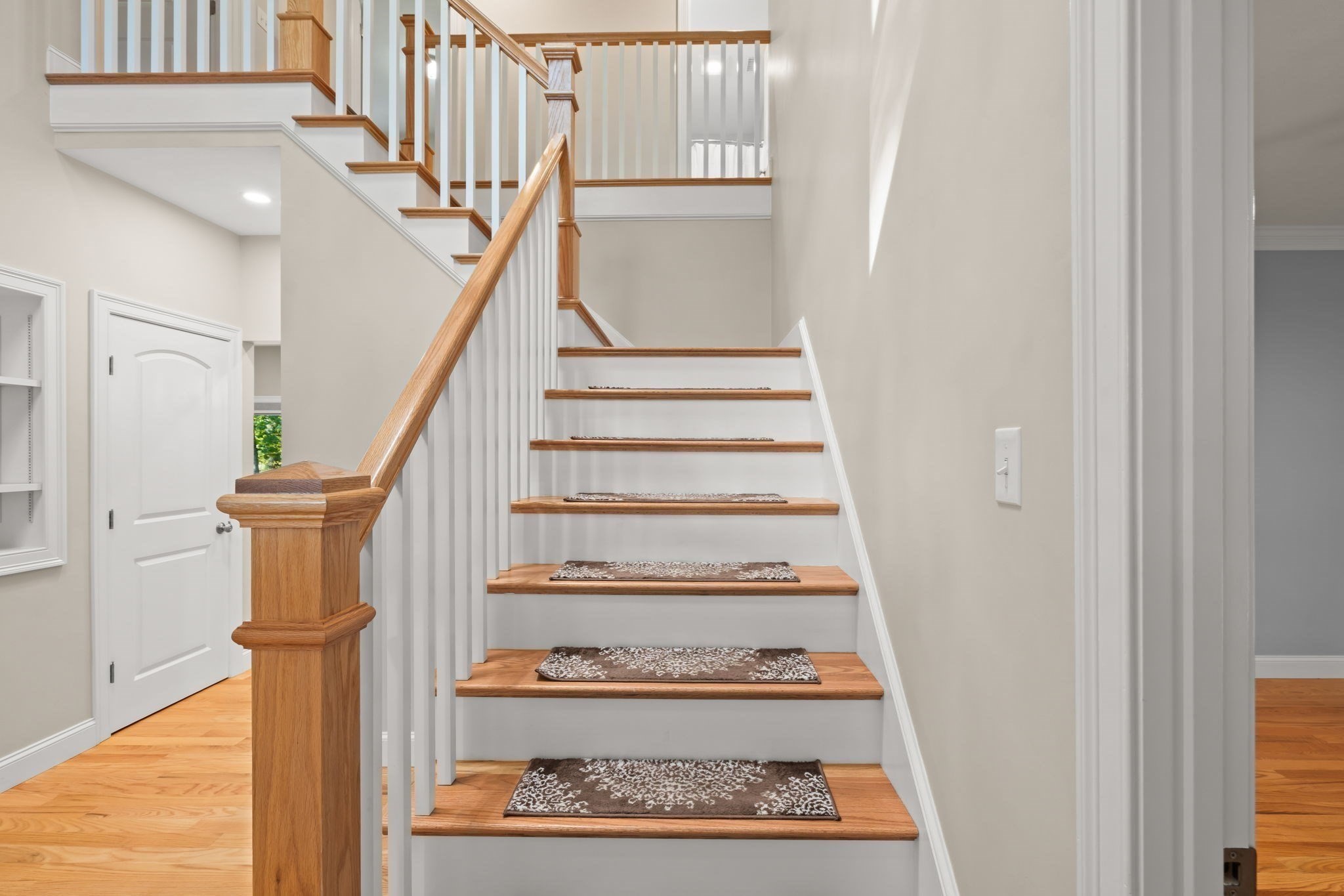 Interior staircase with warm wood treads, white balusters, and patterned runners.