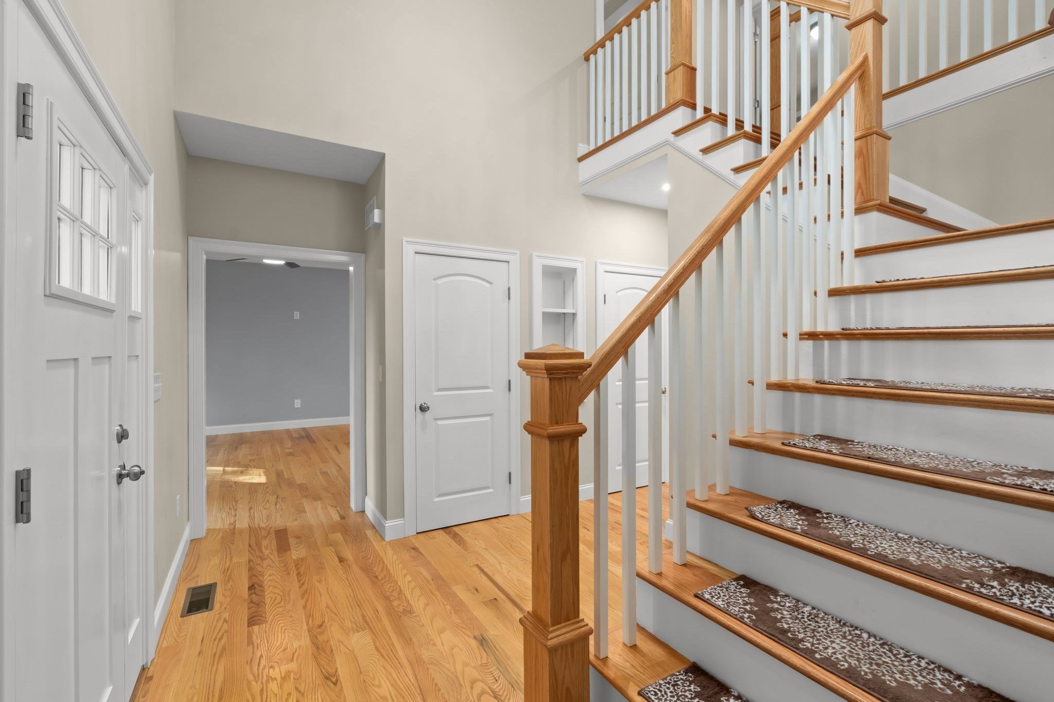 Entry hall with hardwood floors and a wood-and-white staircase with patterned stair runners.