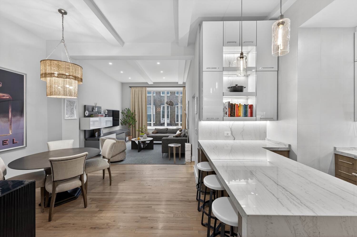Open-plan kitchen and living area with a long marble island, white cabinetry, and wood floors.