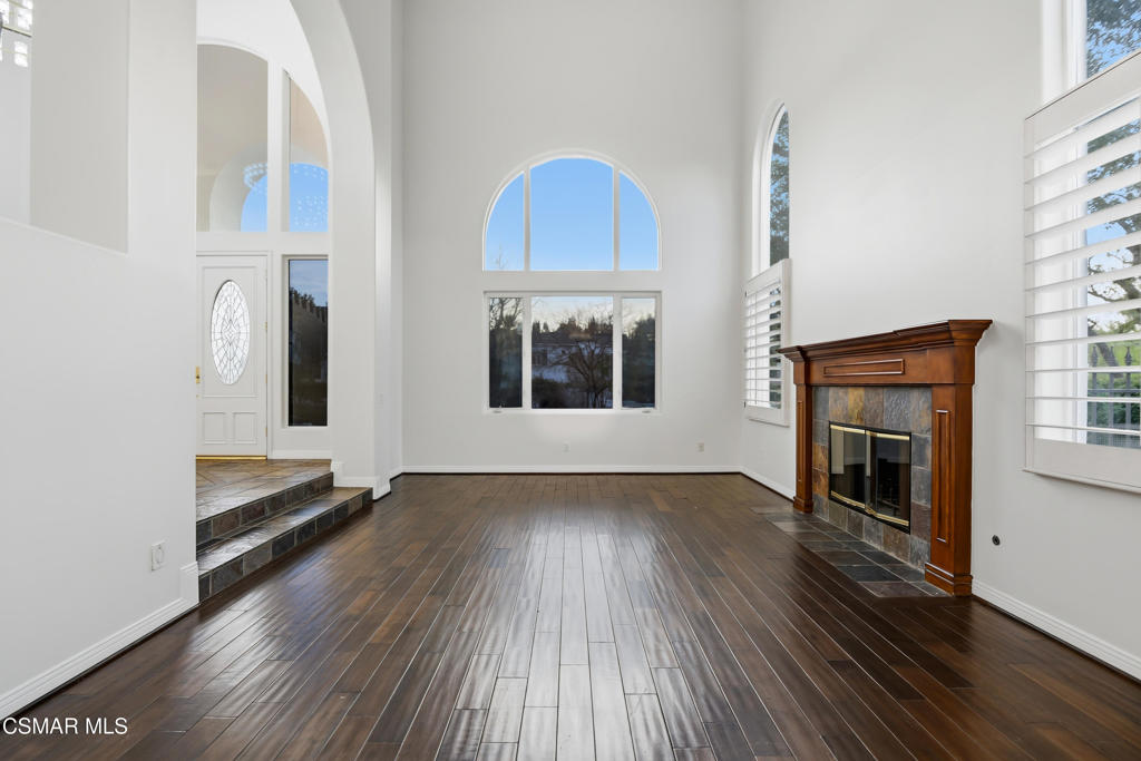 Vacant living room with arched windows, dark hardwood floors, and a wood-trimmed fireplace.