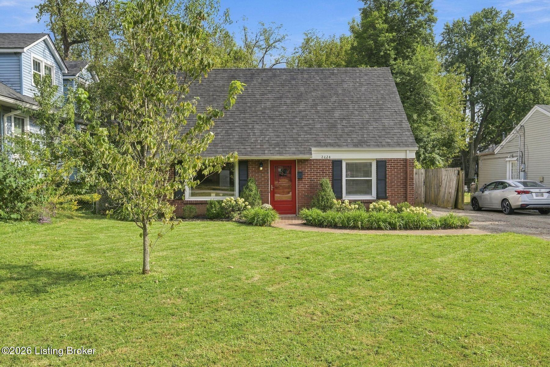 Brick house with a red front door, steep roof, and landscaped lawn.
