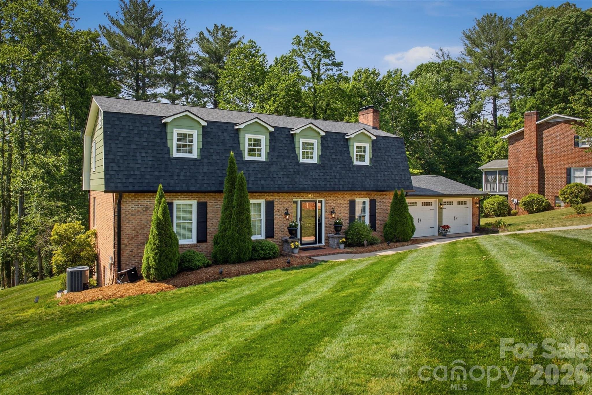 Brick house with four roof dormers, an attached two-car garage, and a broad sloping lawn.